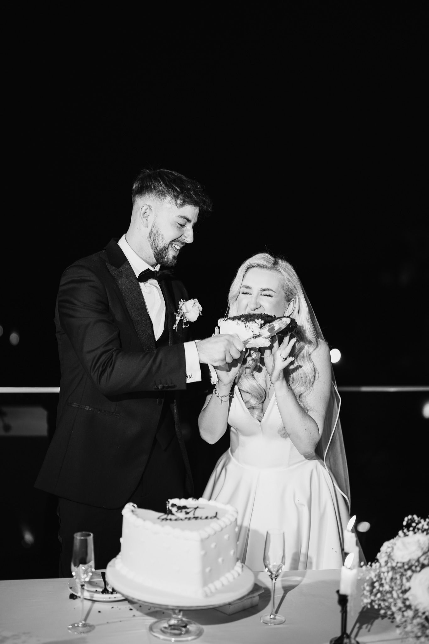 Wedding couple playfully feeds each other cake during traditional cake cutting ceremony.