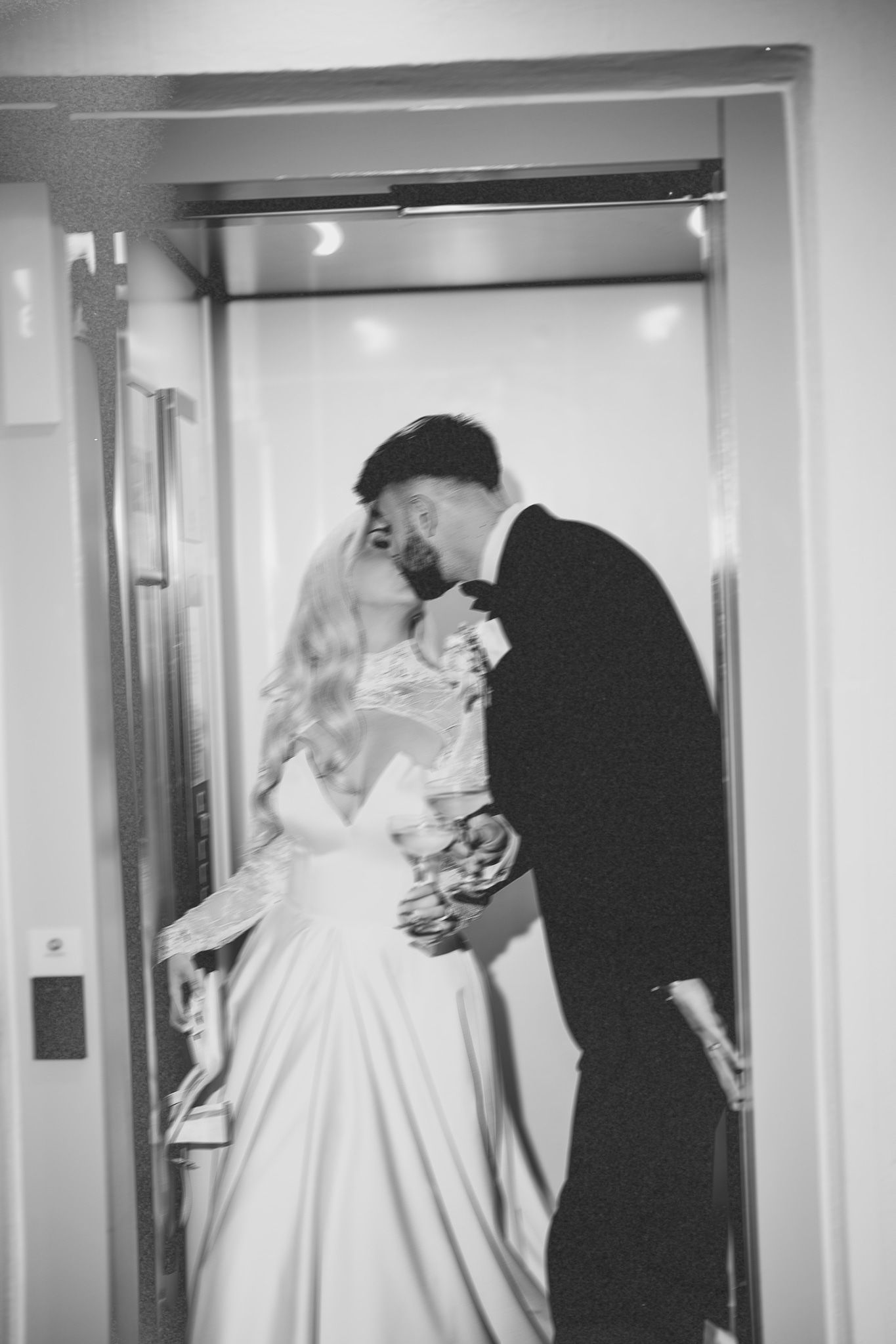 Black and white photograph captures bride and groom in elevator moments.