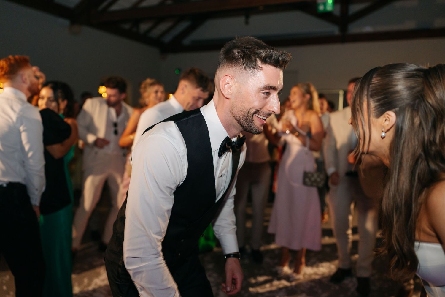 Wedding guests enjoying a lively dance party in an indoor venue.