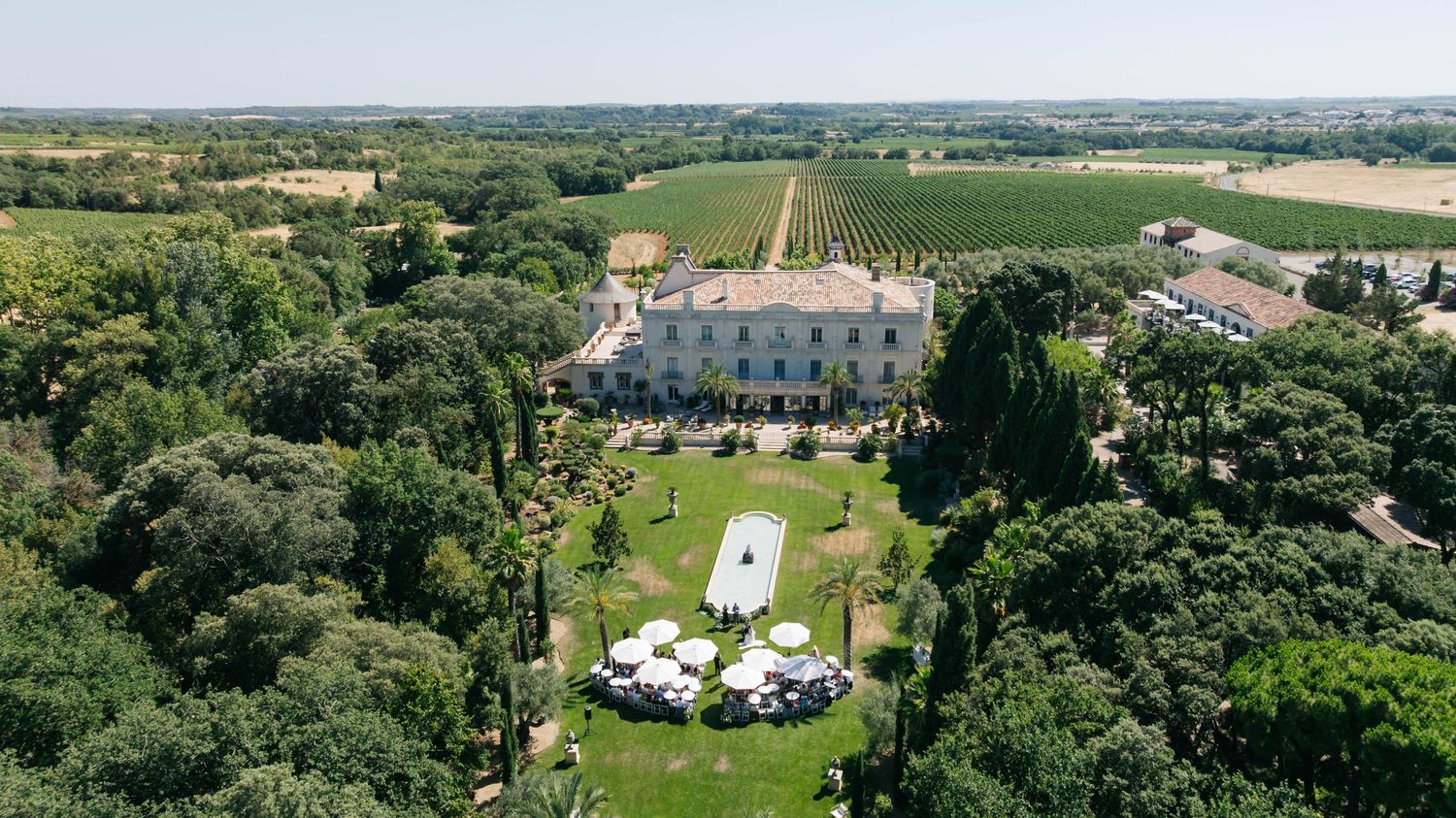 Aerial view of an elegant French chateau surrounded by lush vineyards, manicured gardens, and white event tents.