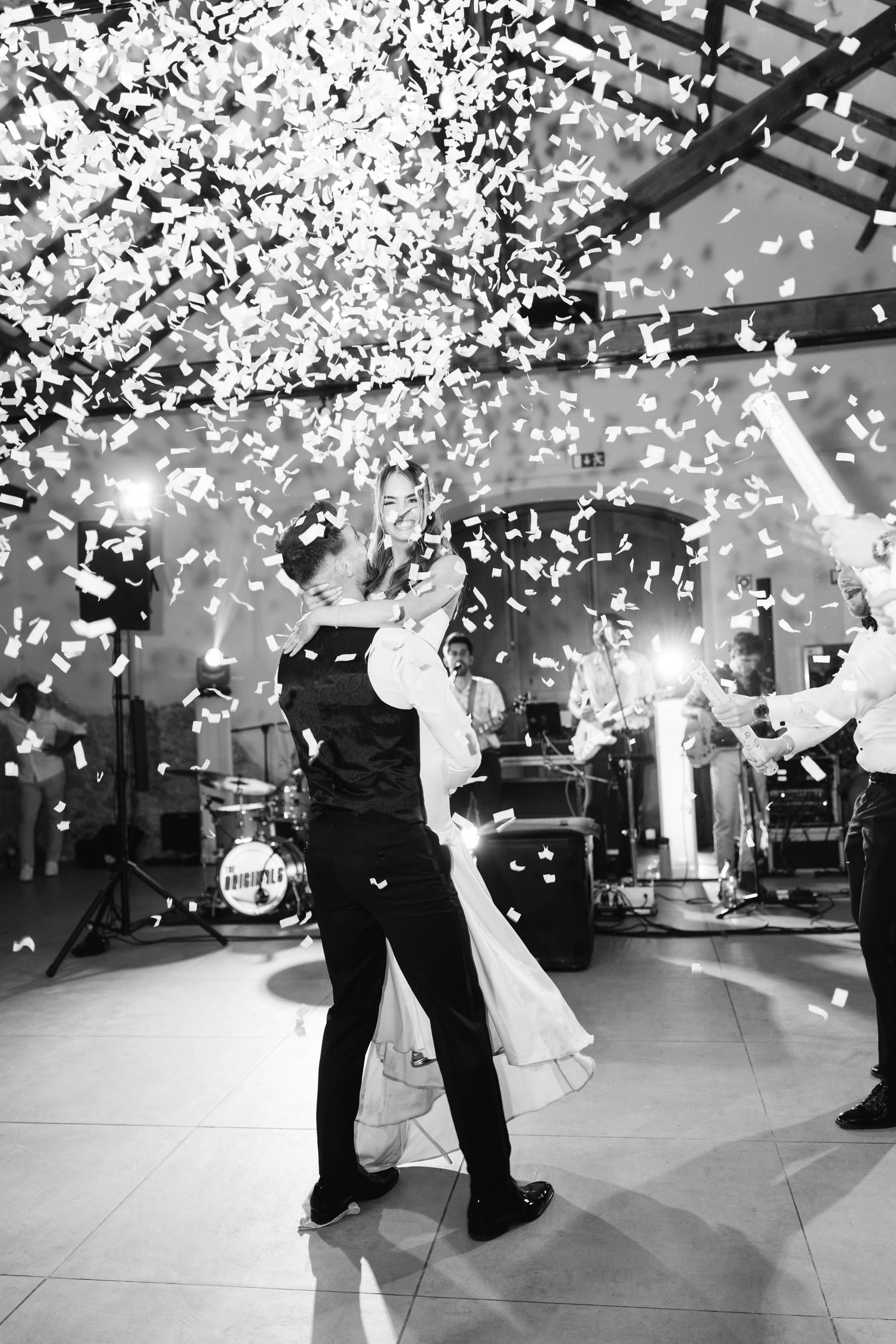 Dancing couple celebrates under shower of white confetti during wedding reception.