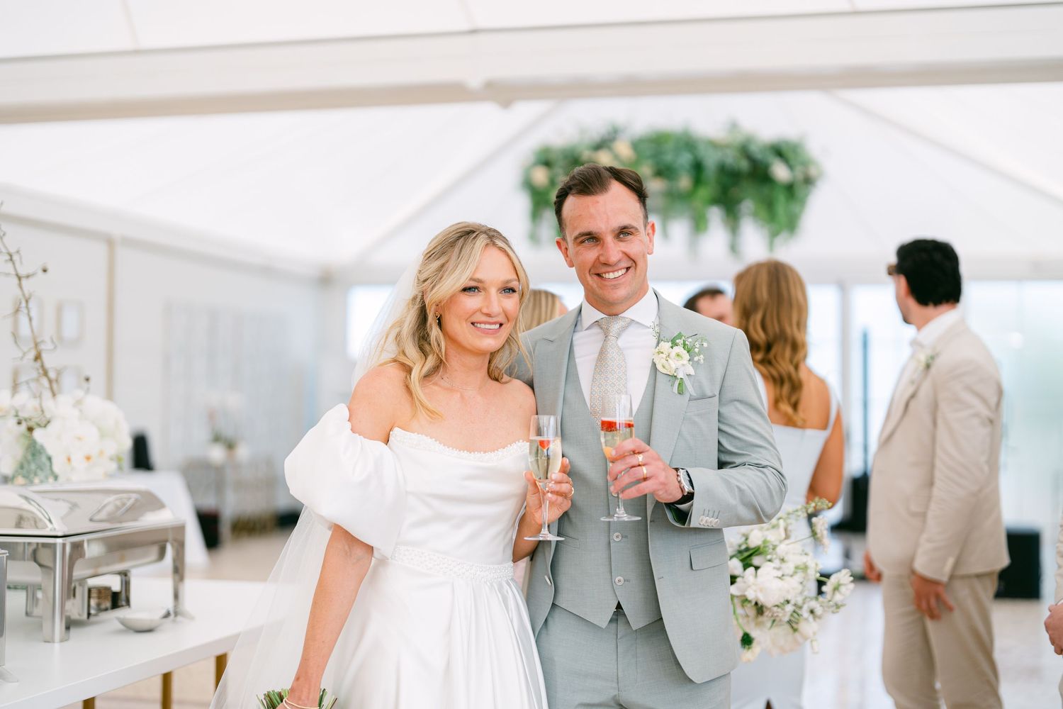 Wedding reception setup with elegant decor and guests mingling under white tent.