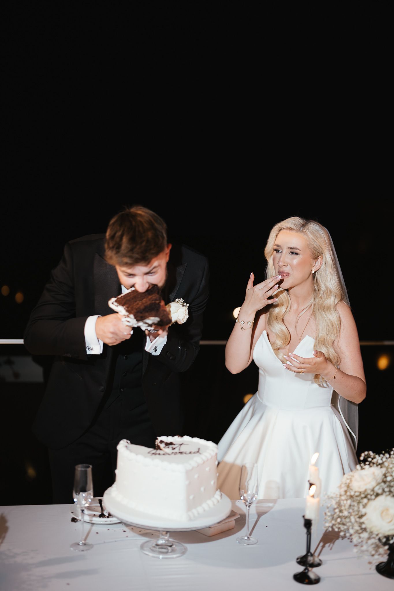 Couple messily enjoying their wedding cake with playful expressions.