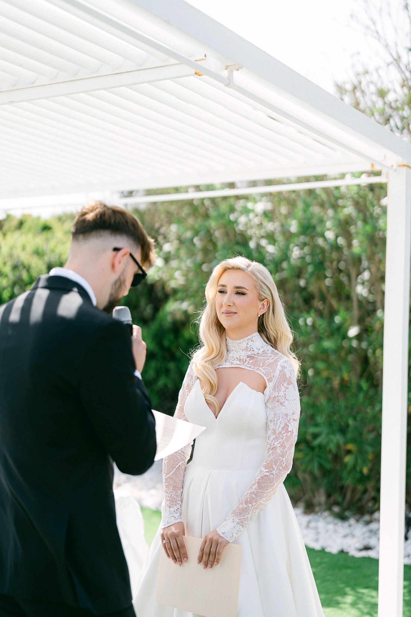 First look wedding moment under white pergola with green garden backdrop.