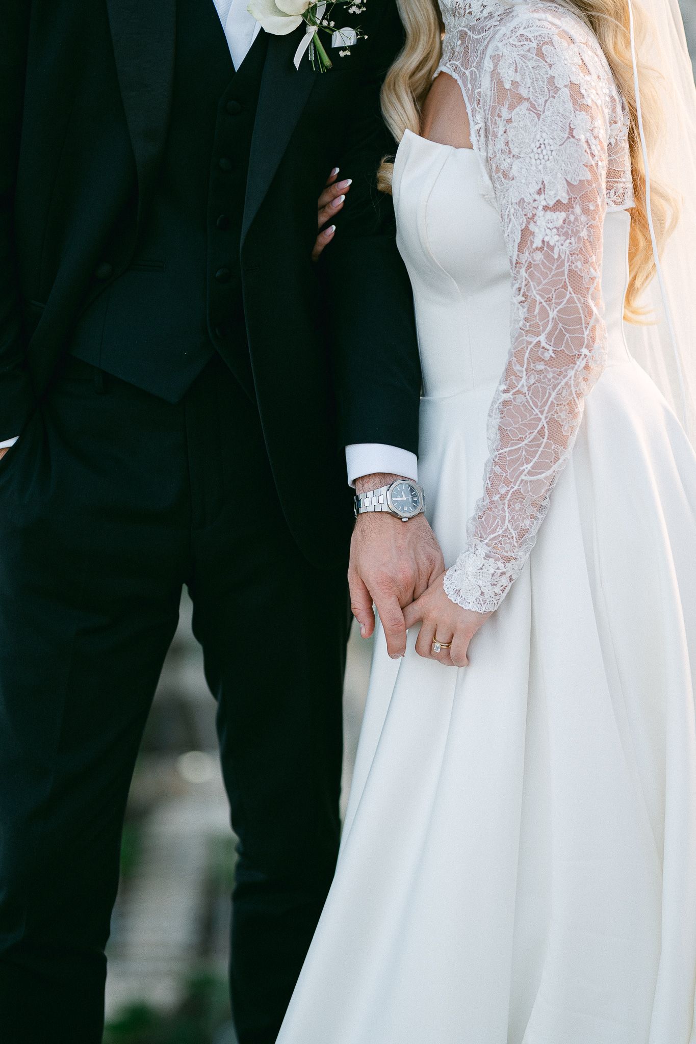 Close-up details of bride's lace sleeve gown next to groom's classic black tuxedo.