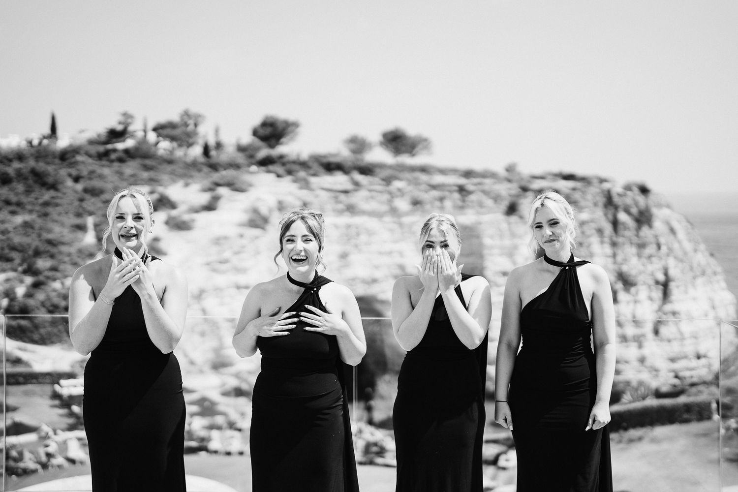 Four bridesmaids in black dresses pose for a black and white photo against rocky cliffs.