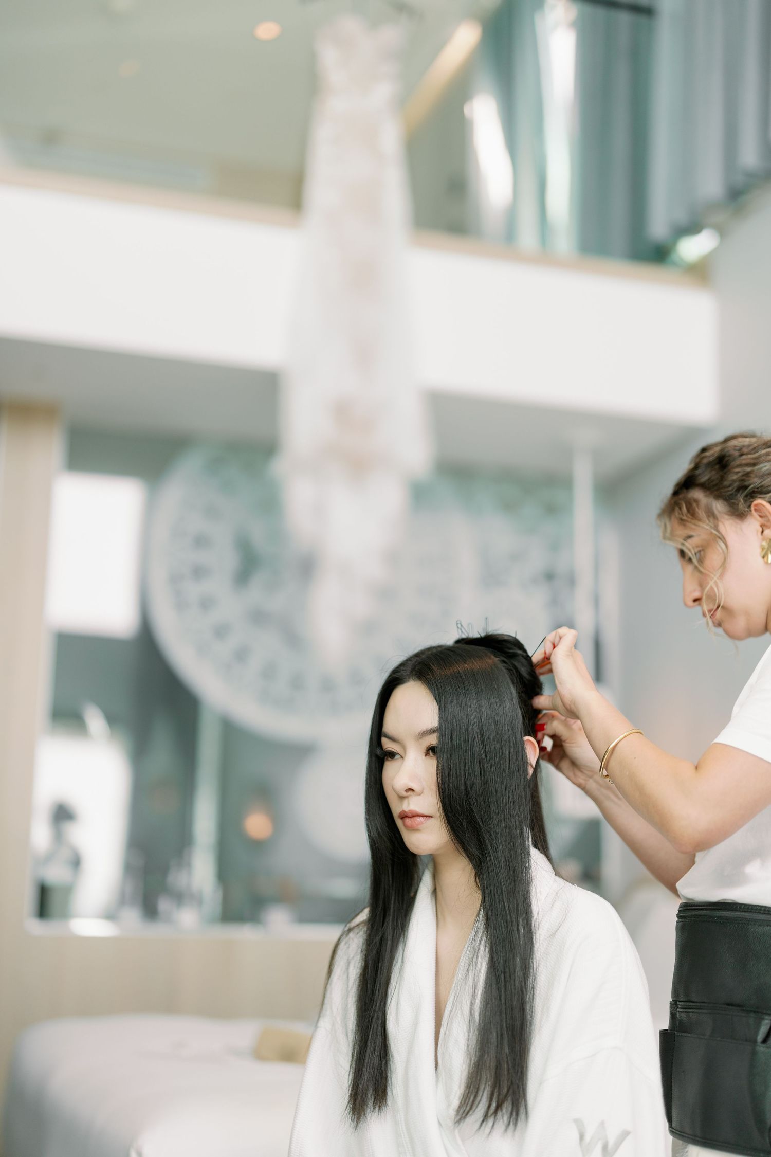 Hair styling session in bright modern room with wedding dress displayed.