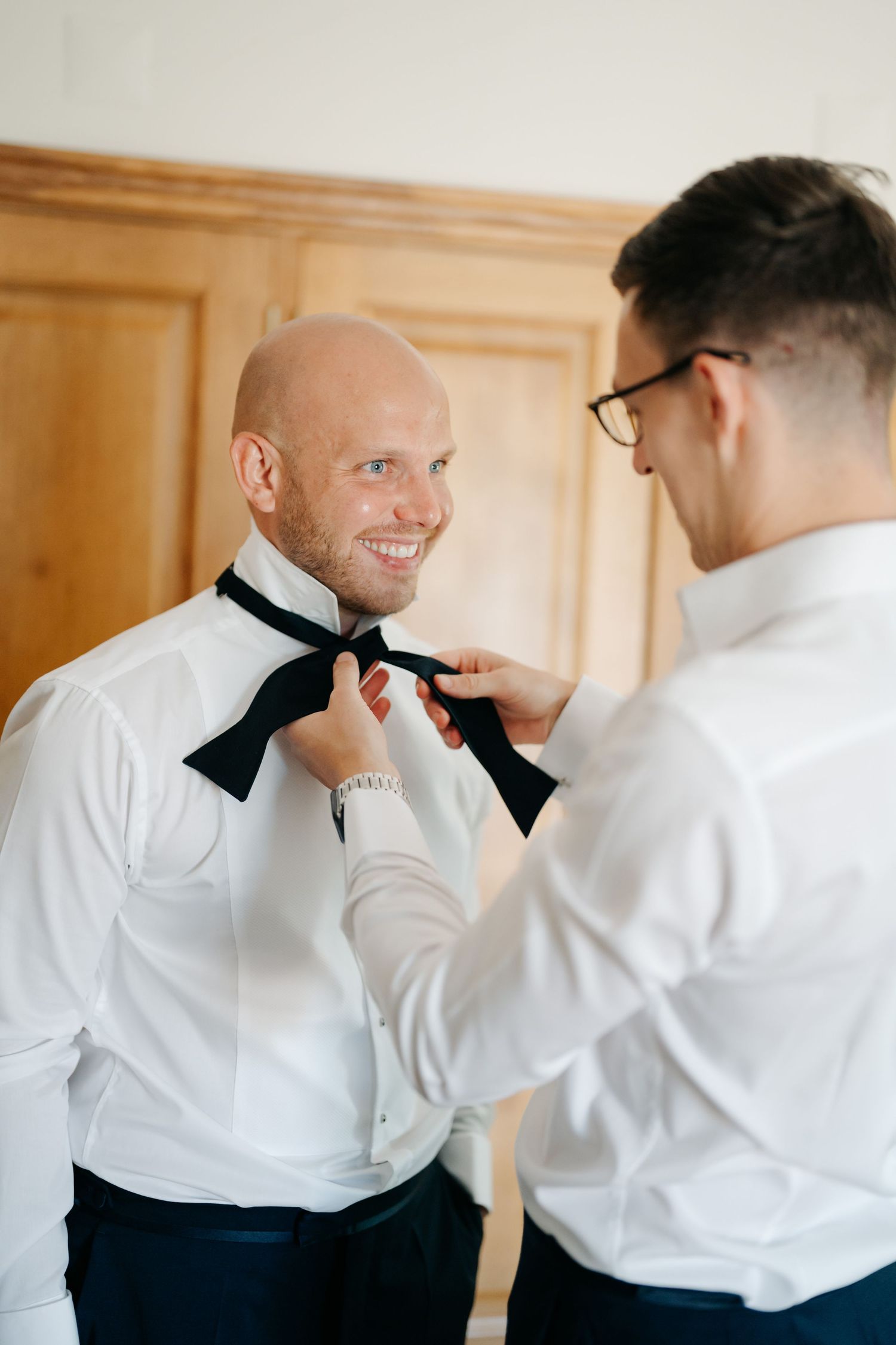 Groomsmen assisting with formal bow tie preparations before ceremony.