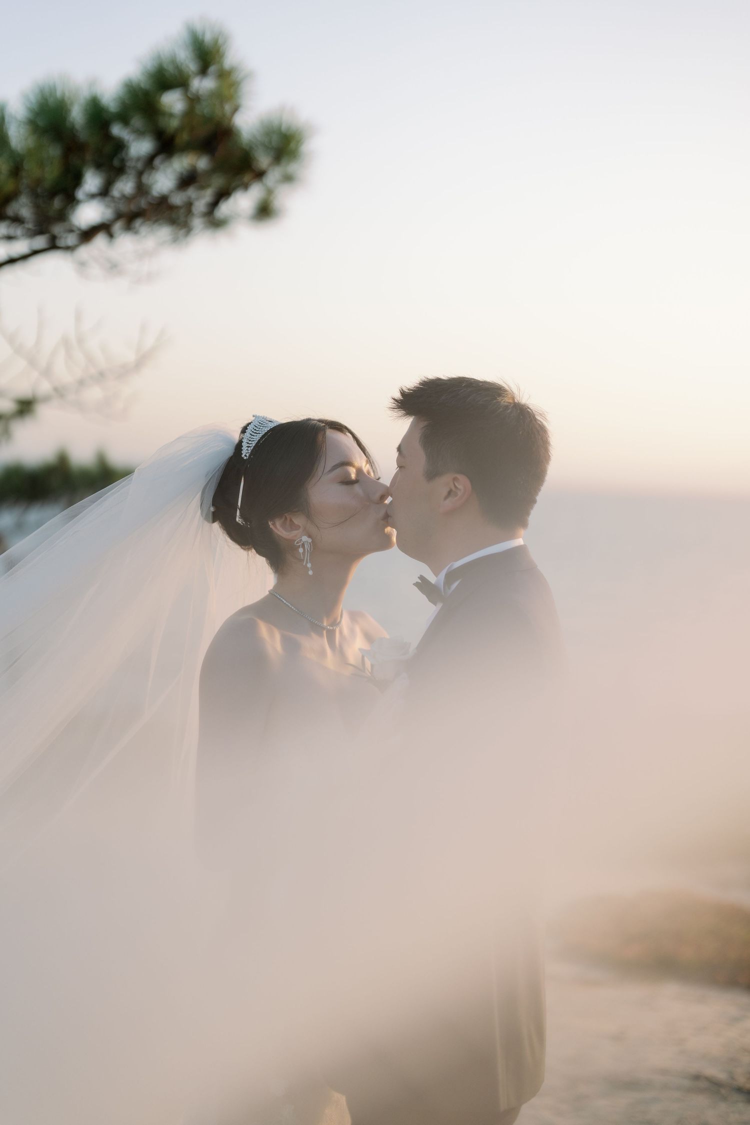 Dreamy wedding couple portrait through sheer veil during sunset.