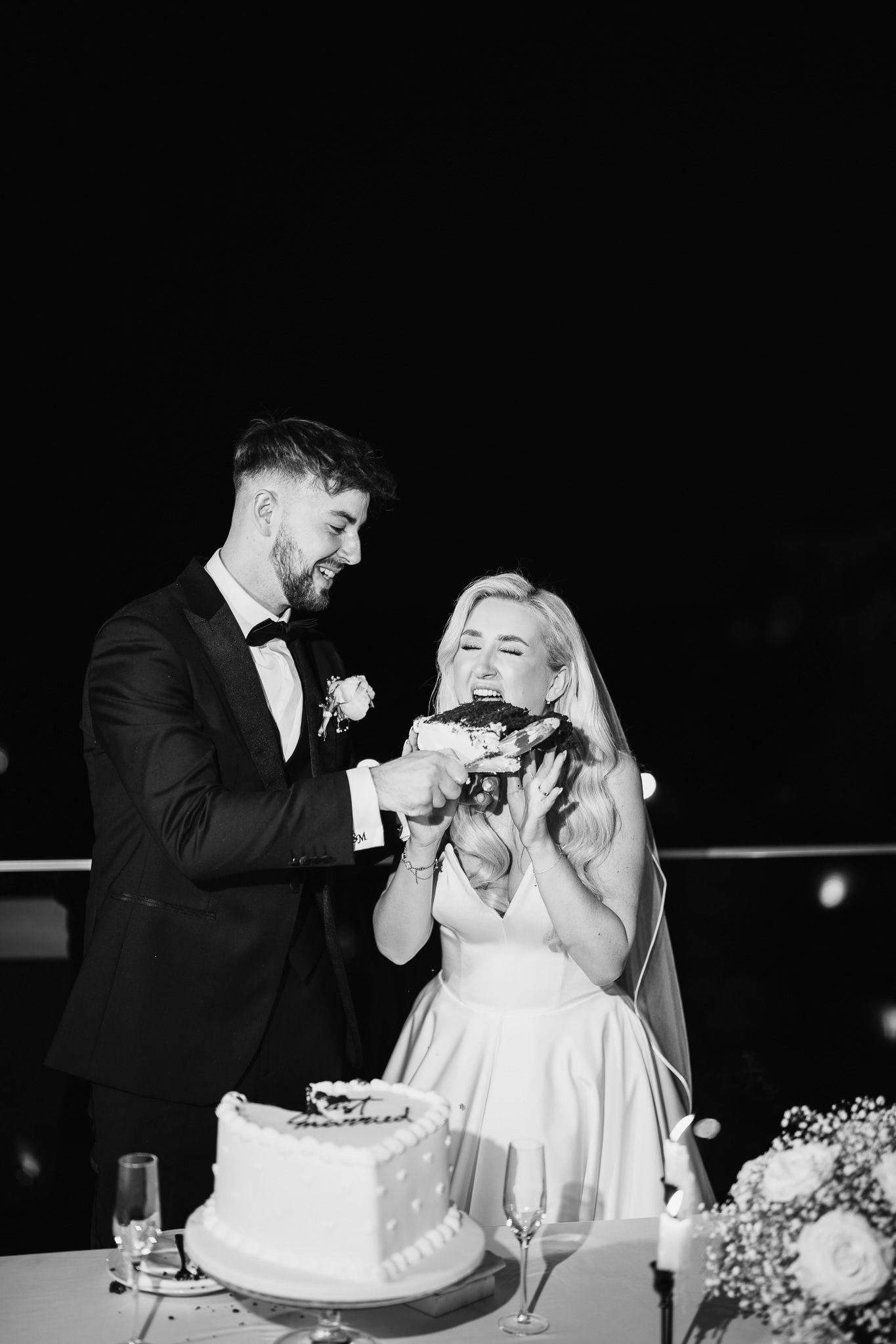 Black and white photo of newlyweds sharing cake at their wedding reception.