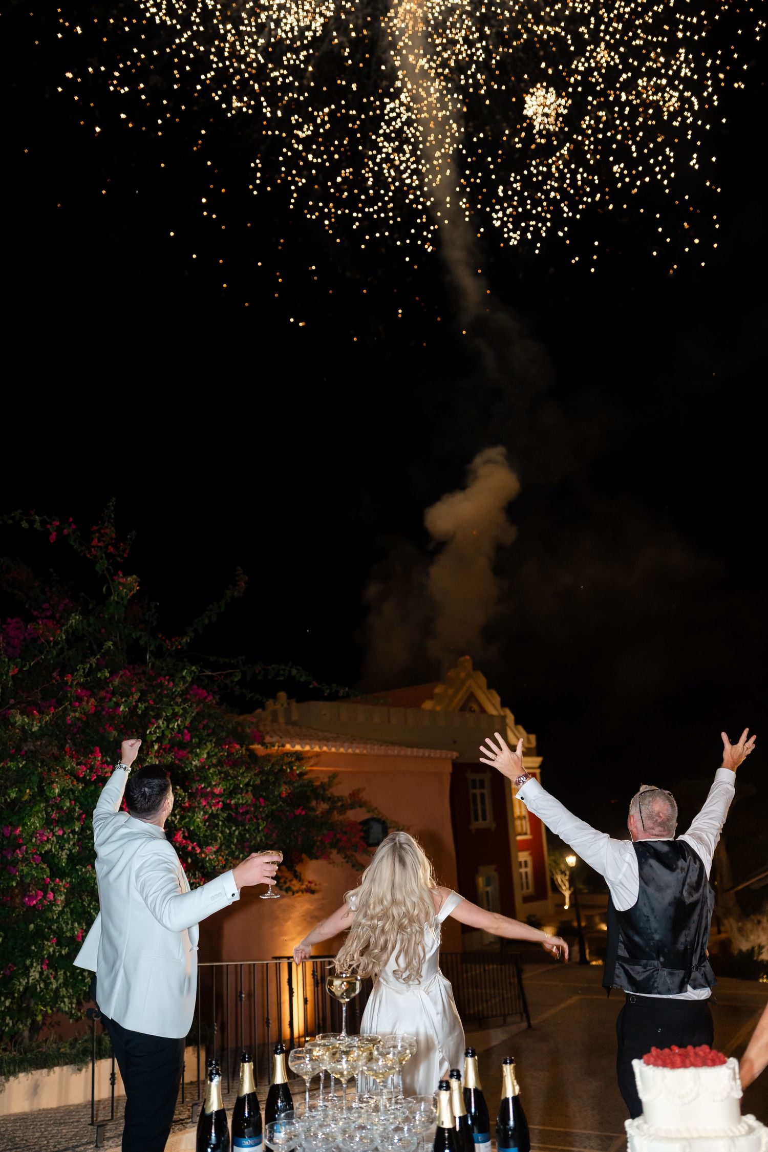 Couple celebrates under sparkling fireworks display at outdoor wedding reception.