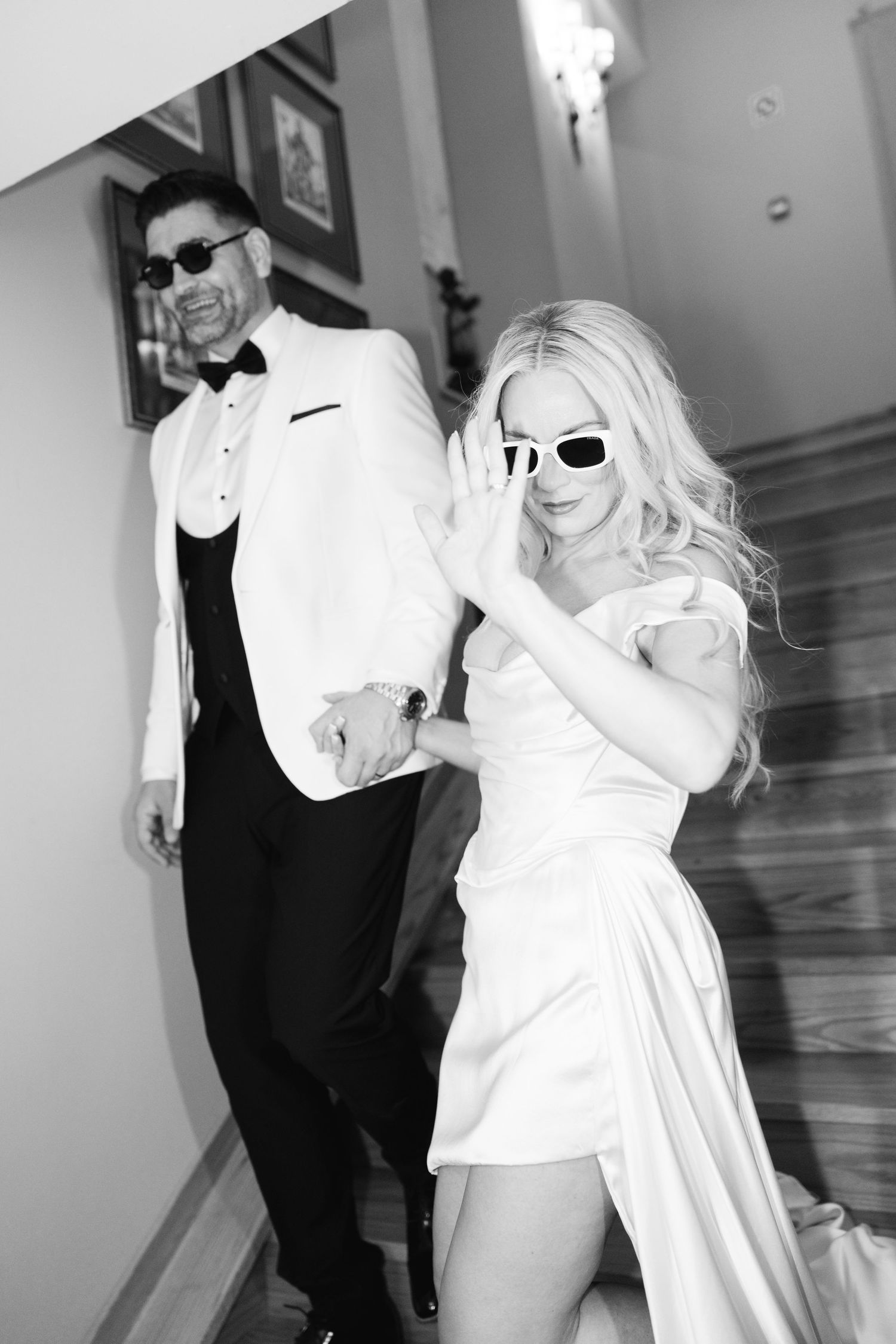 A couple in formal black and white attire dancing playfully in an indoor setting.