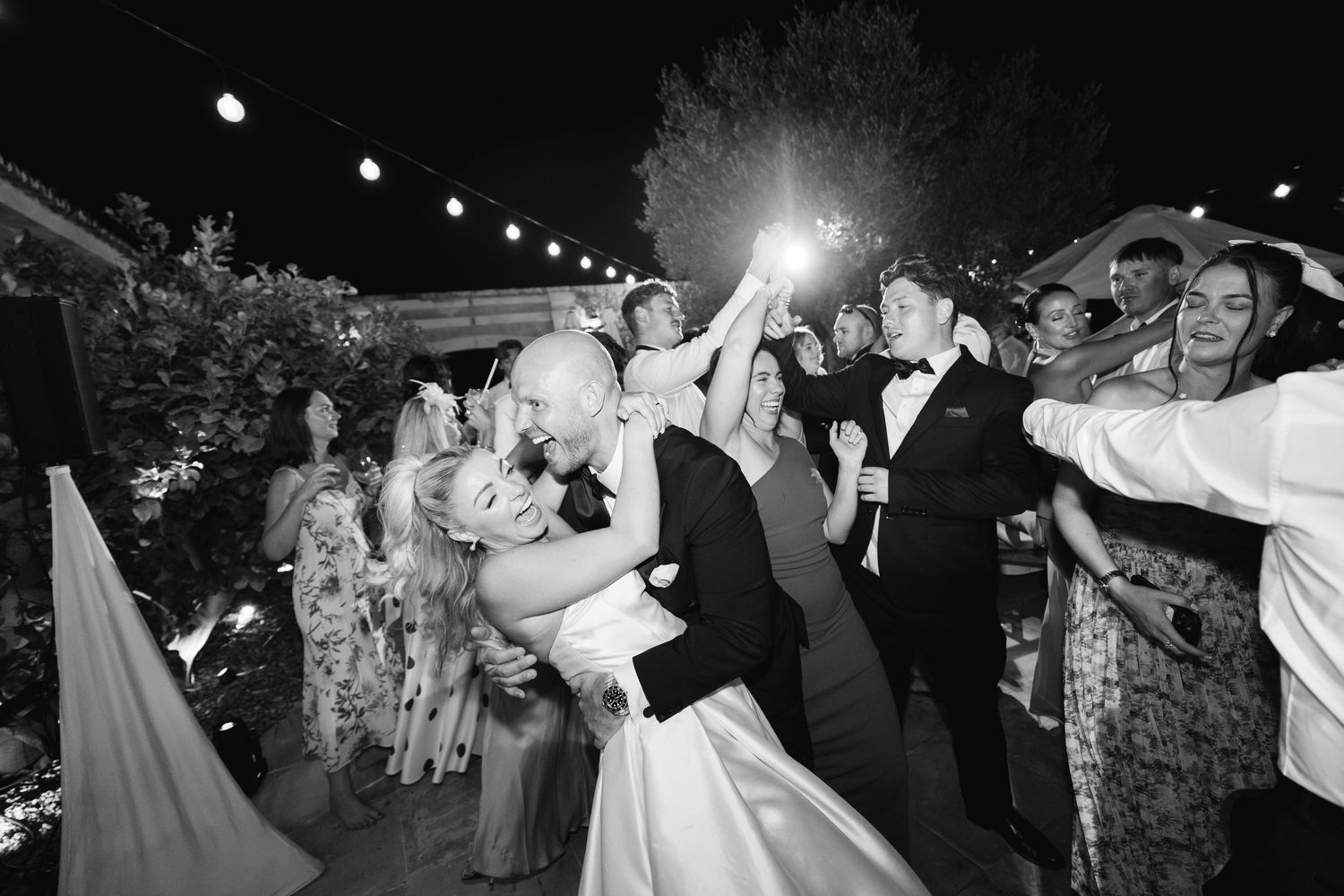 Wedding guests celebrate on the dance floor during an outdoor evening reception.