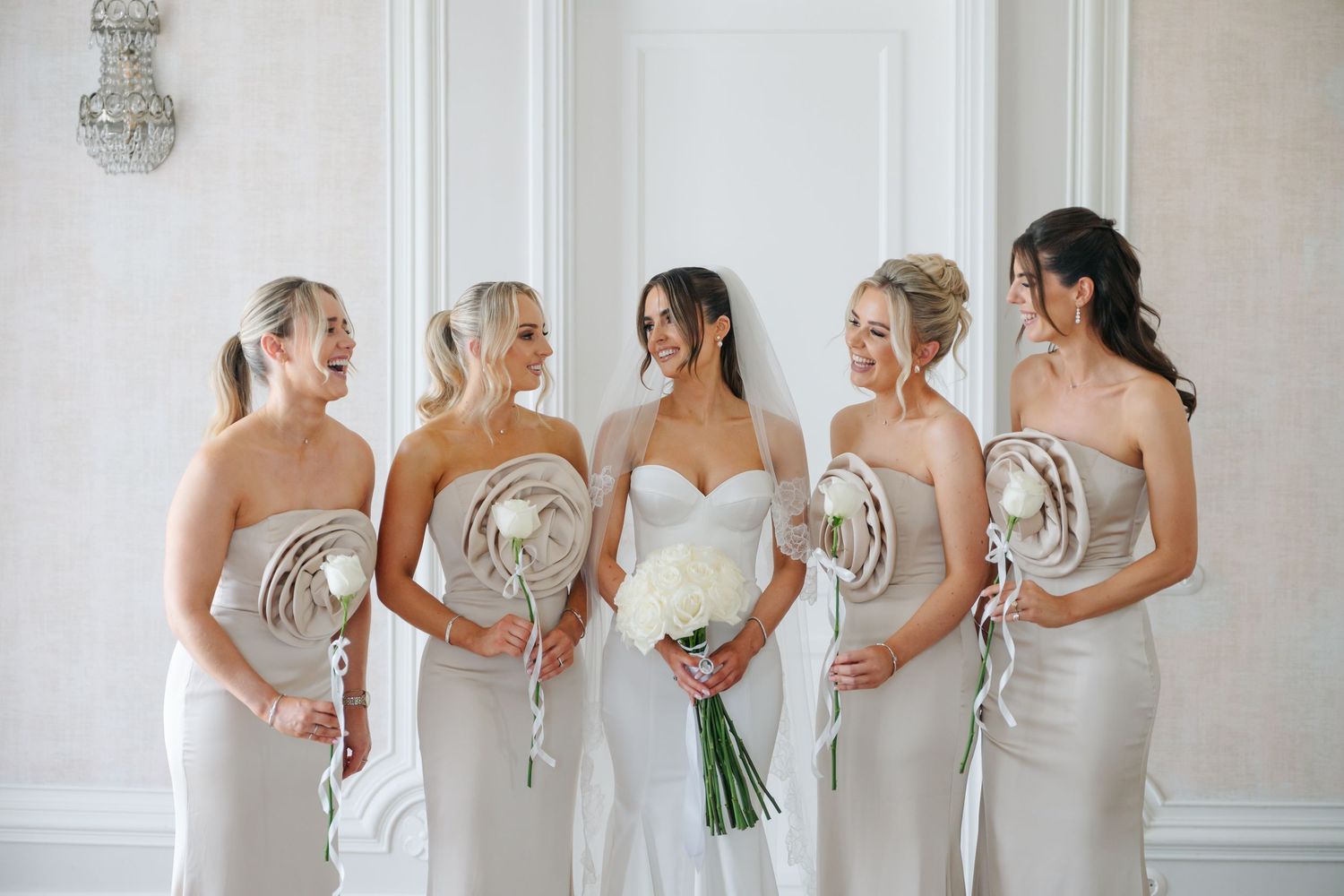 Bridesmaids in matching light-colored dresses stand in a row holding bouquets.