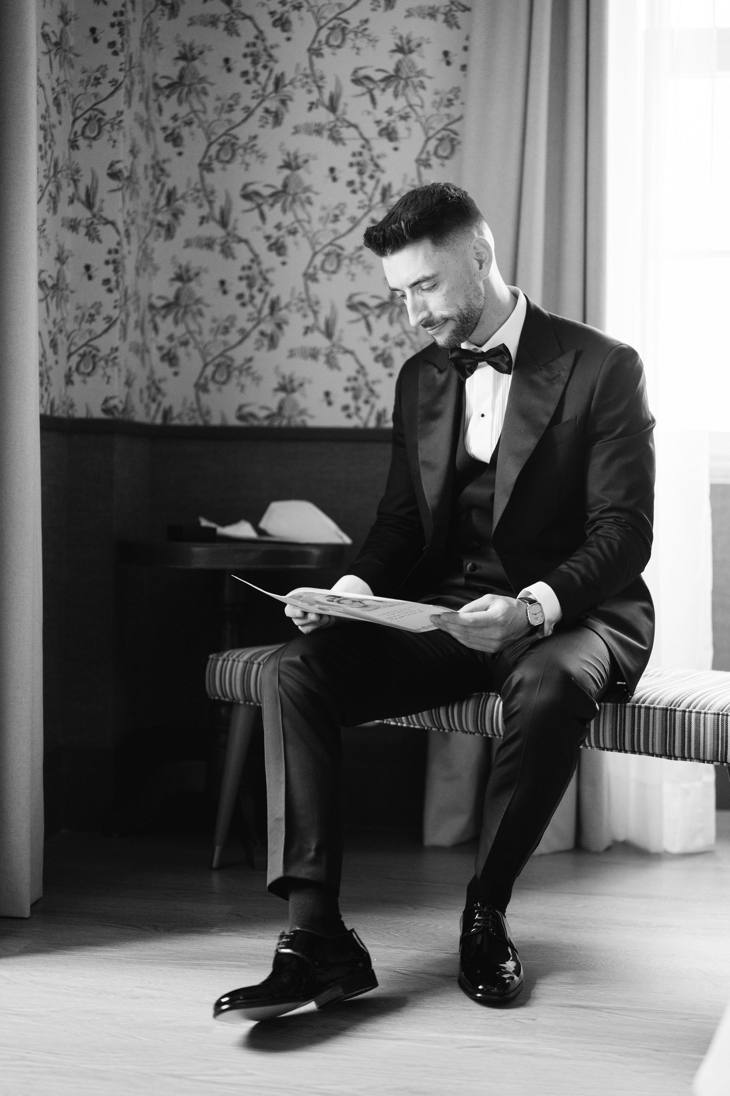 Black and white photo of formal attire while reading document in elegant setting.