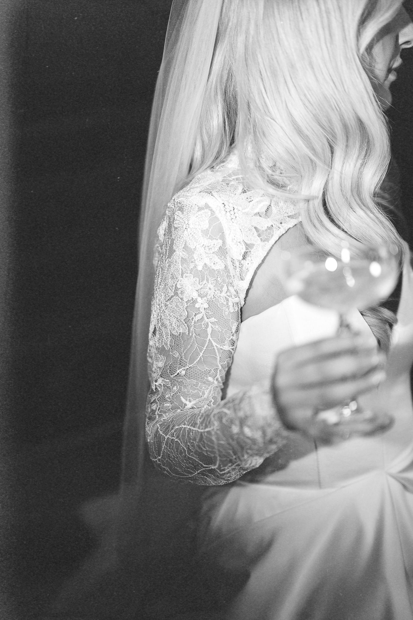 Detailed shot of lace sleeves on a white wedding gown in dramatic lighting.
