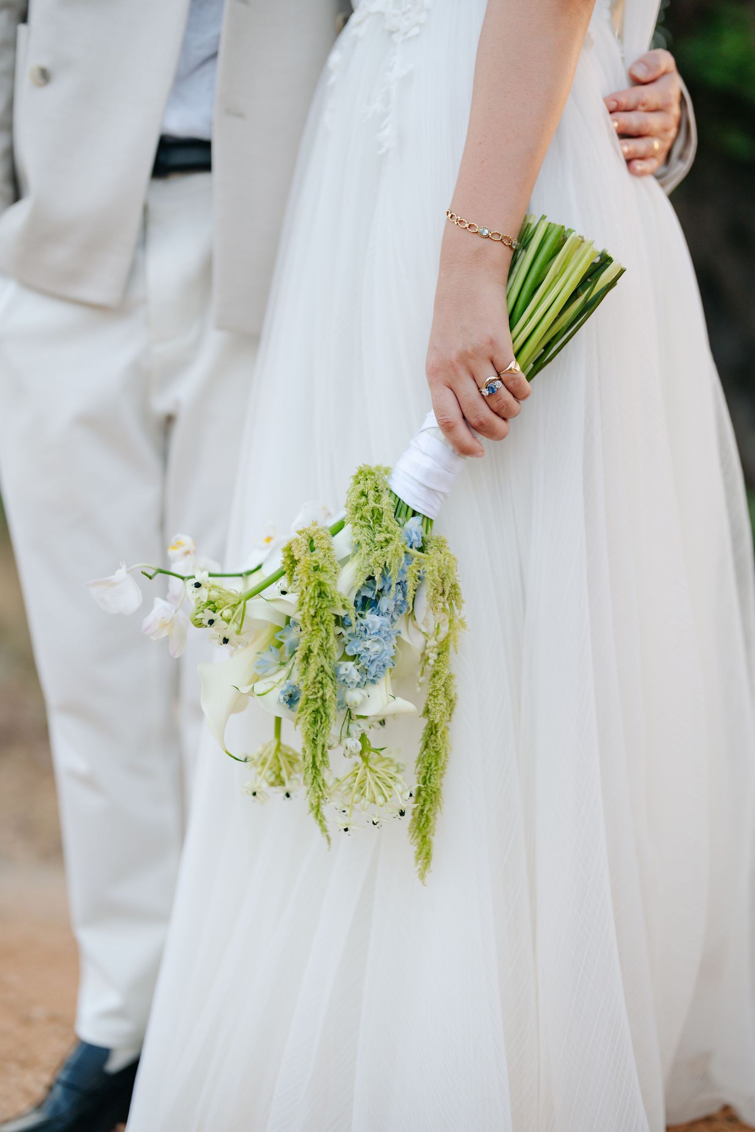 Close-up view of a bride in white dress holding a delicate green and blue floral bouquet during a wedding ceremony.