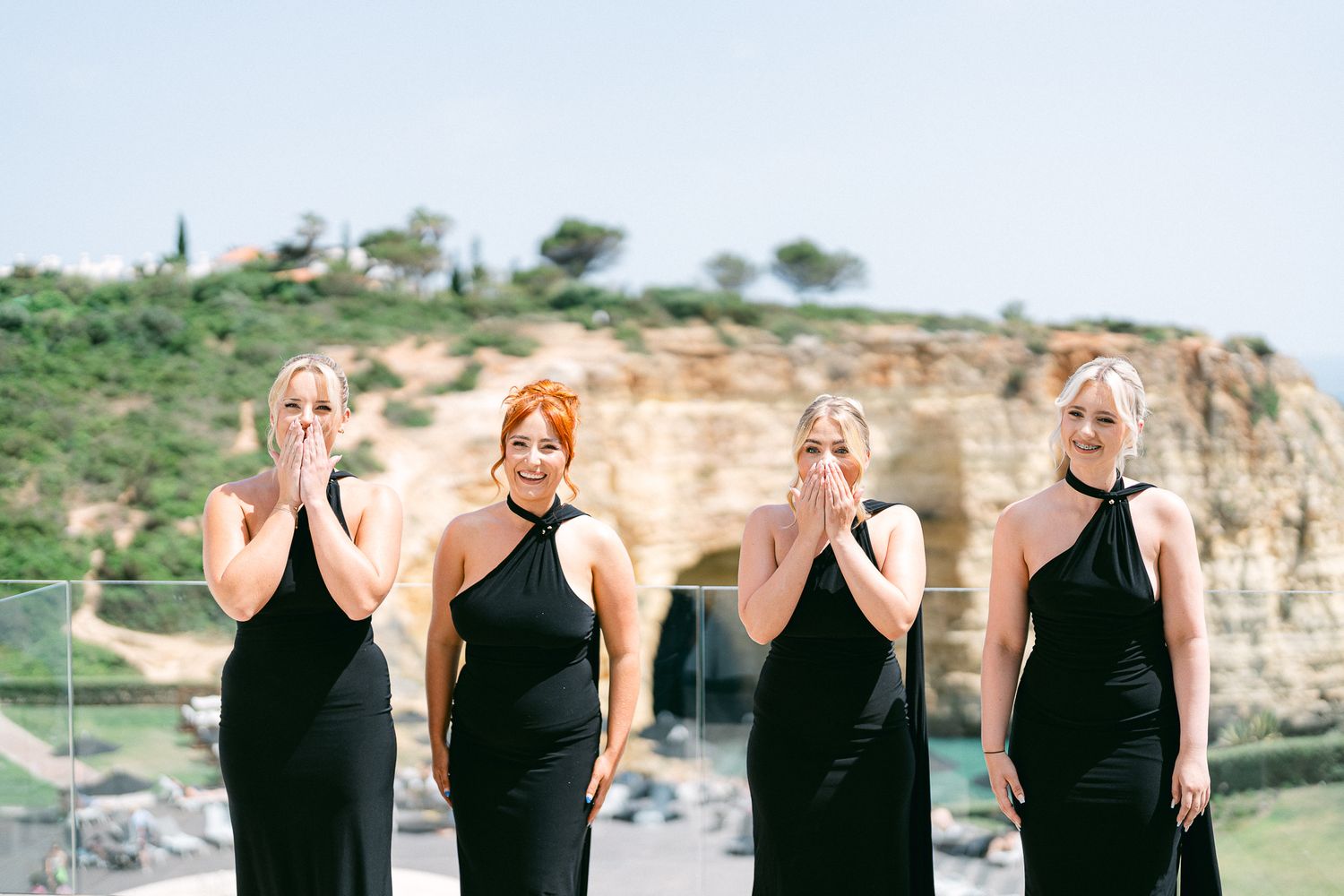 Four bridesmaids in matching black dresses pose against a scenic cliff backdrop.