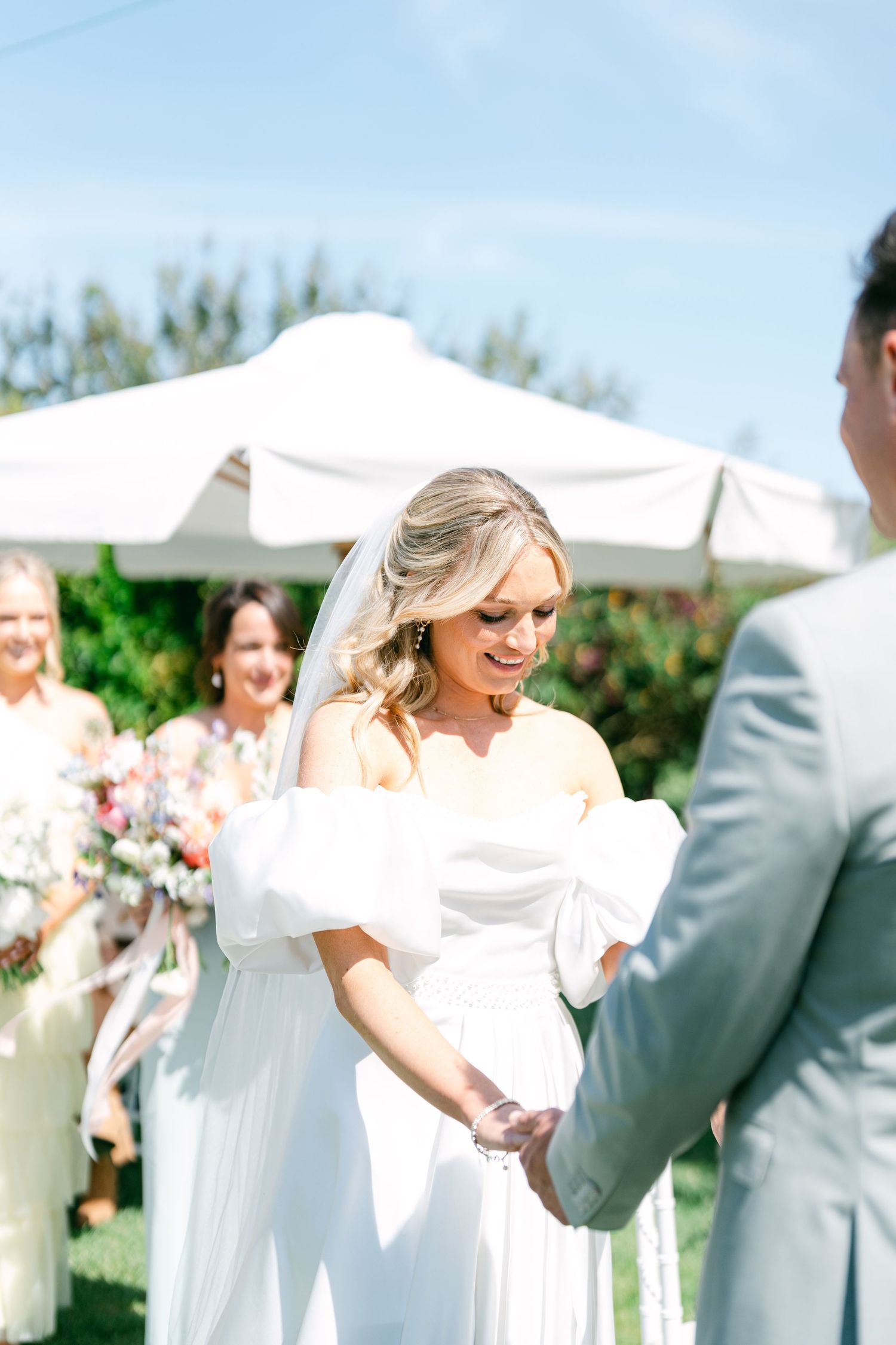 Wedding party celebrates during an outdoor garden ceremony with white tents and floral arrangements.