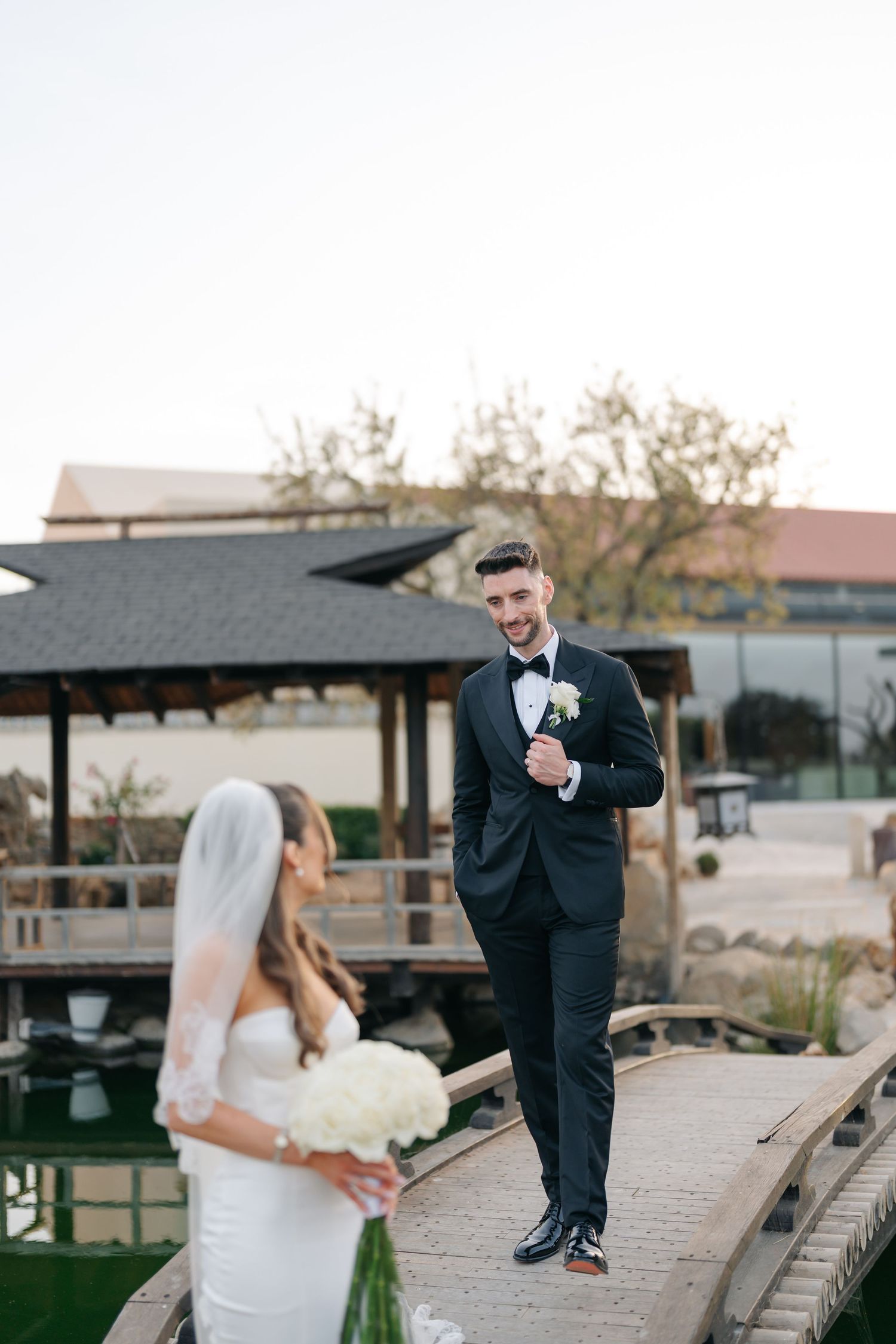 Playful wedding couple interacts on elevated wooden pathway in garden setting.
