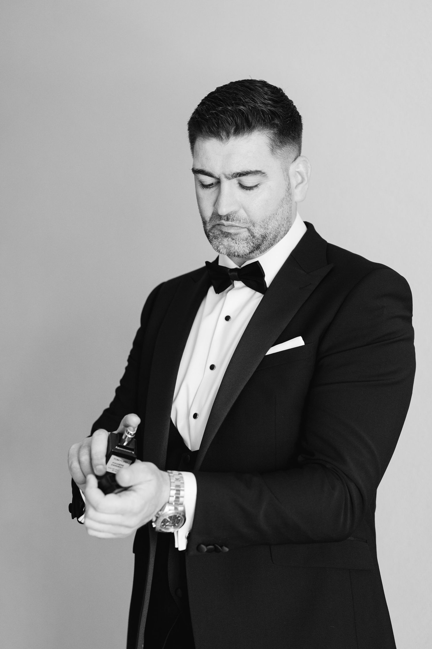 Elegant black and white photo of a groom checking his watch while wearing a classic tuxedo.
