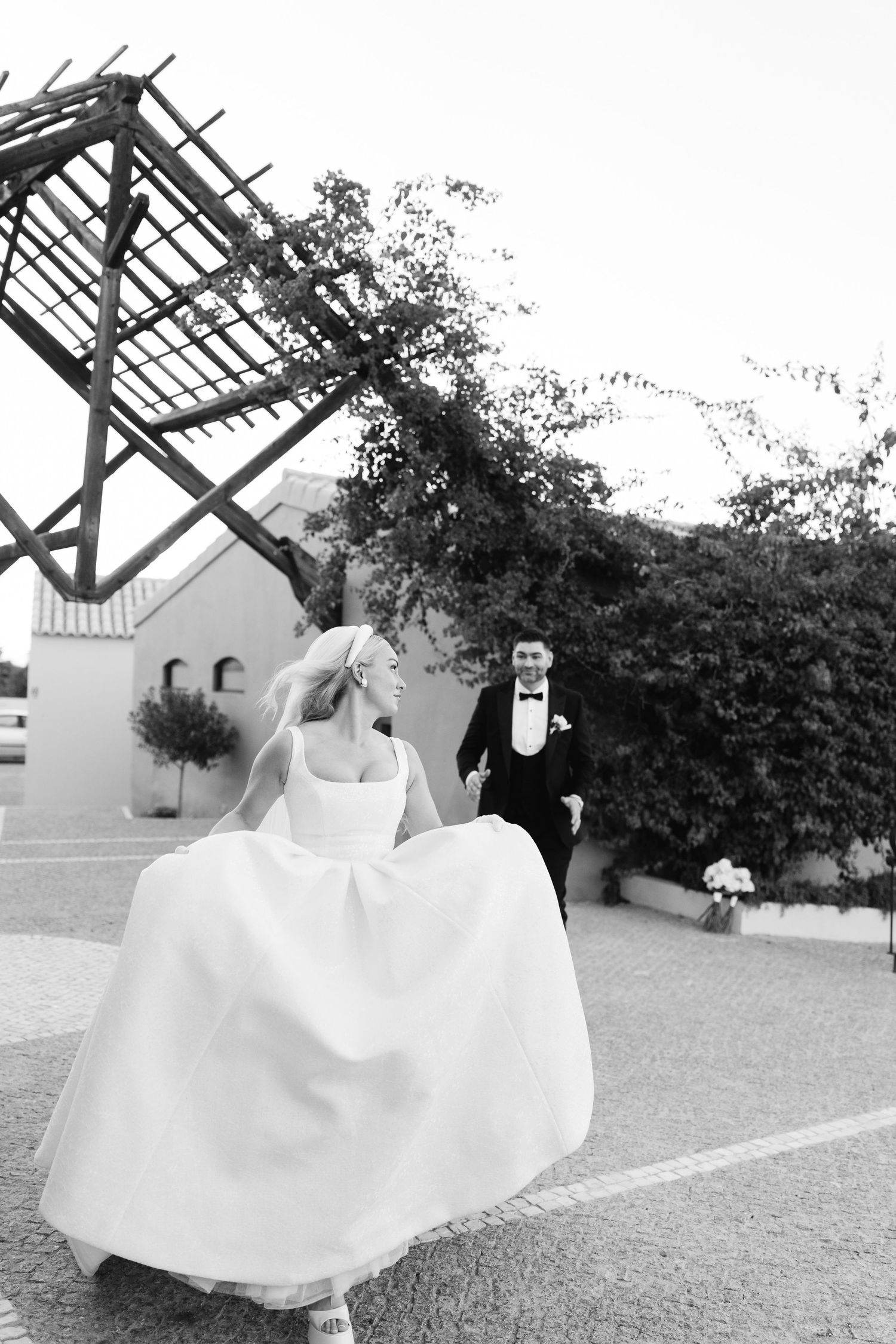 Bride in flowing white dress running playfully through a garden setting.