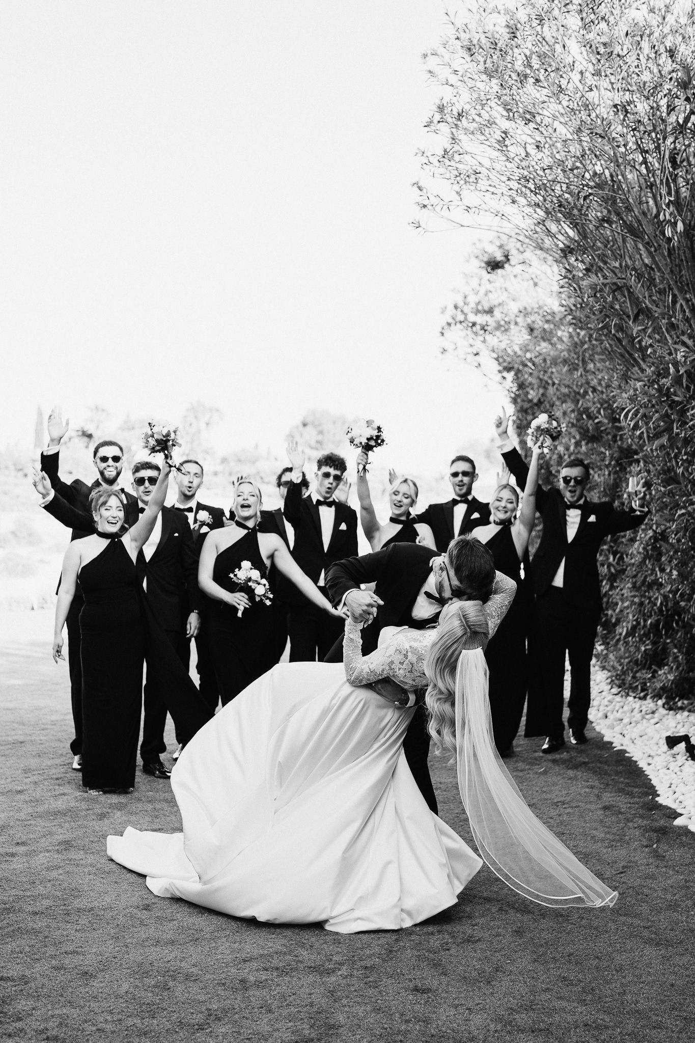 Wedding group creates dynamic poses with flowing dresses against natural outdoor backdrop.