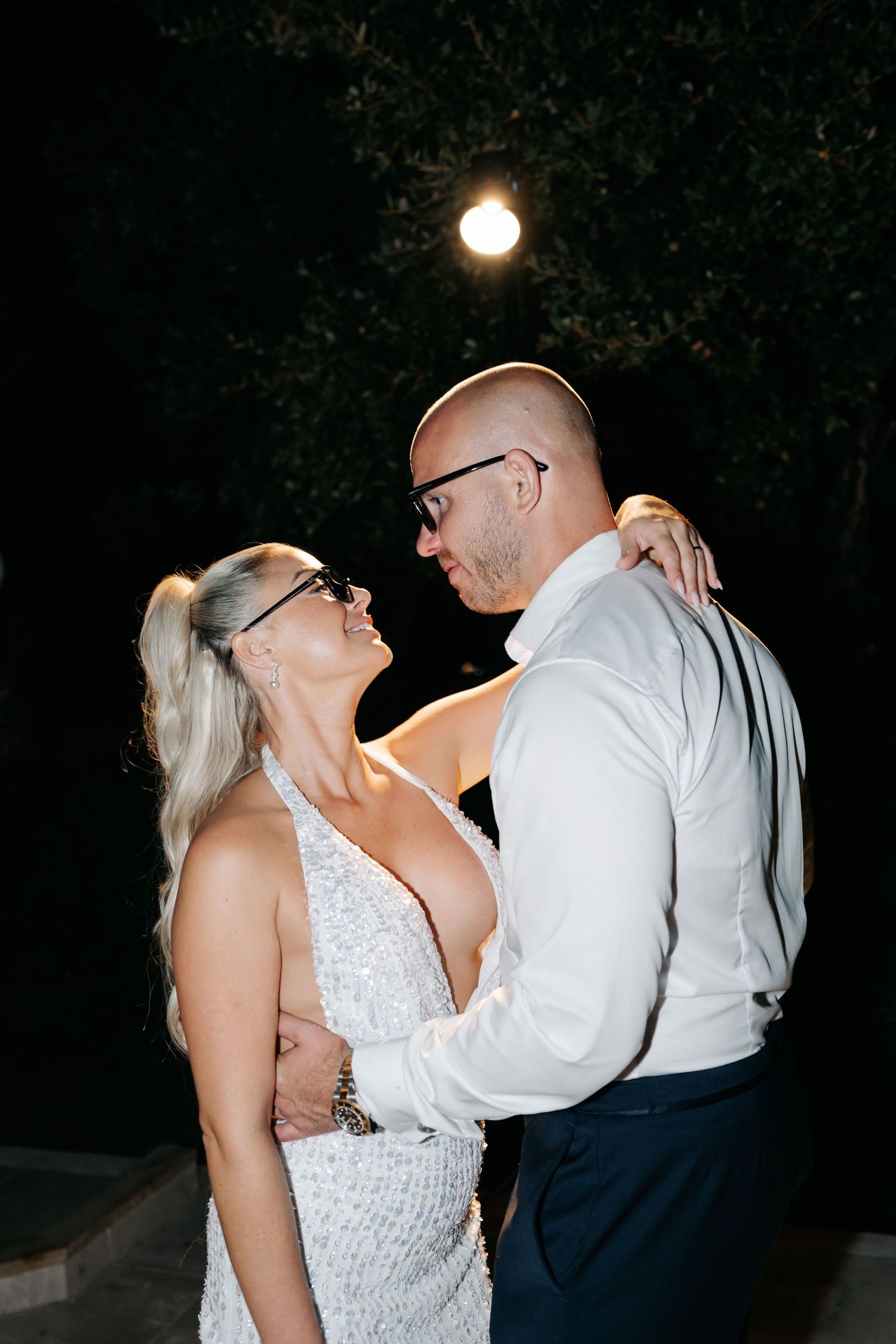 Couple in formal attire dancing intimately at night under outdoor lighting.