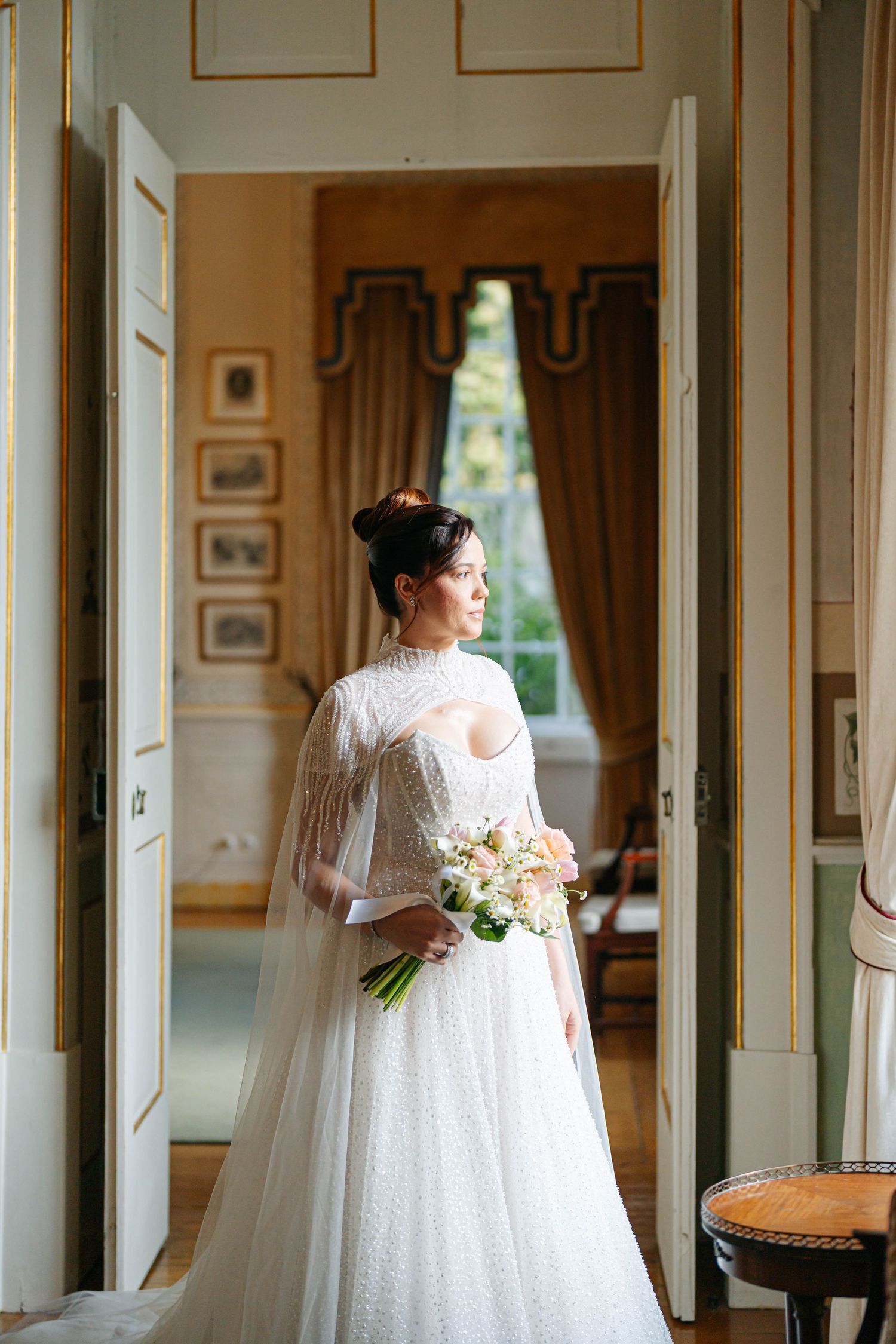 Elegant hallway with ornate gold trim and natural lighting featuring white wedding attire.
