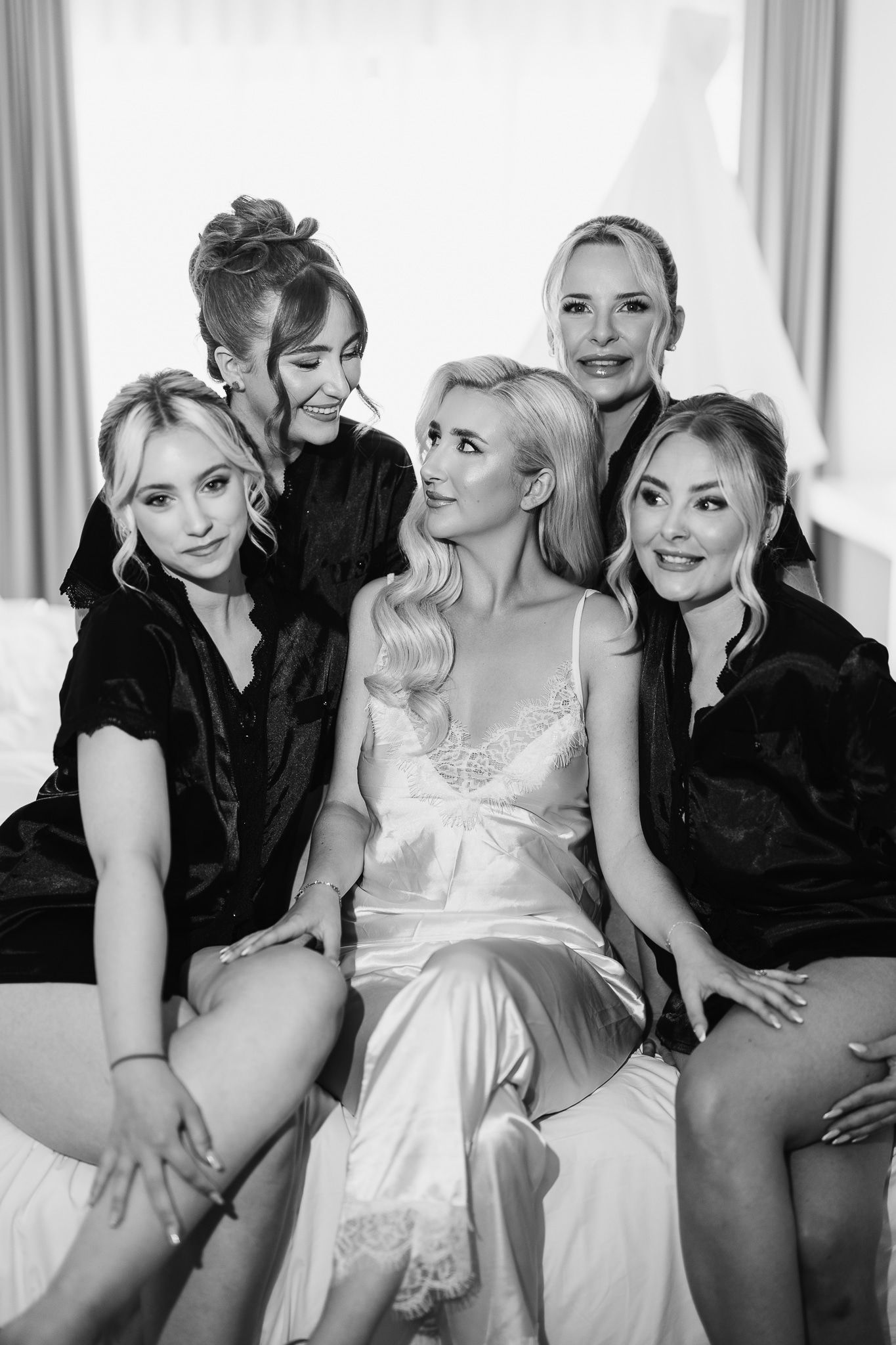 Black and white photo of a bridal party lounging and laughing together on a couch.