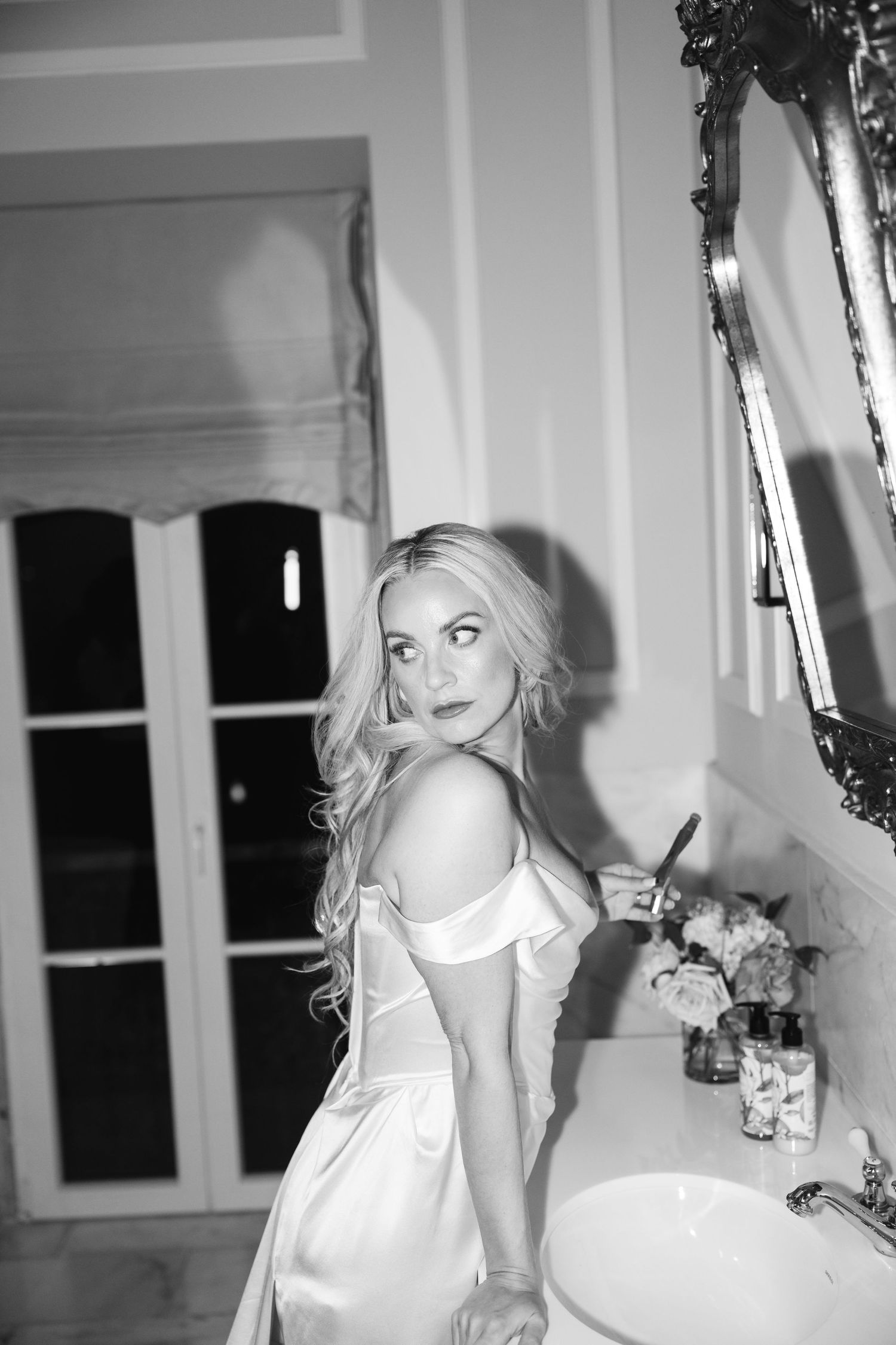 Black and white portrait in luxurious bathroom with ornate gold-framed mirror.