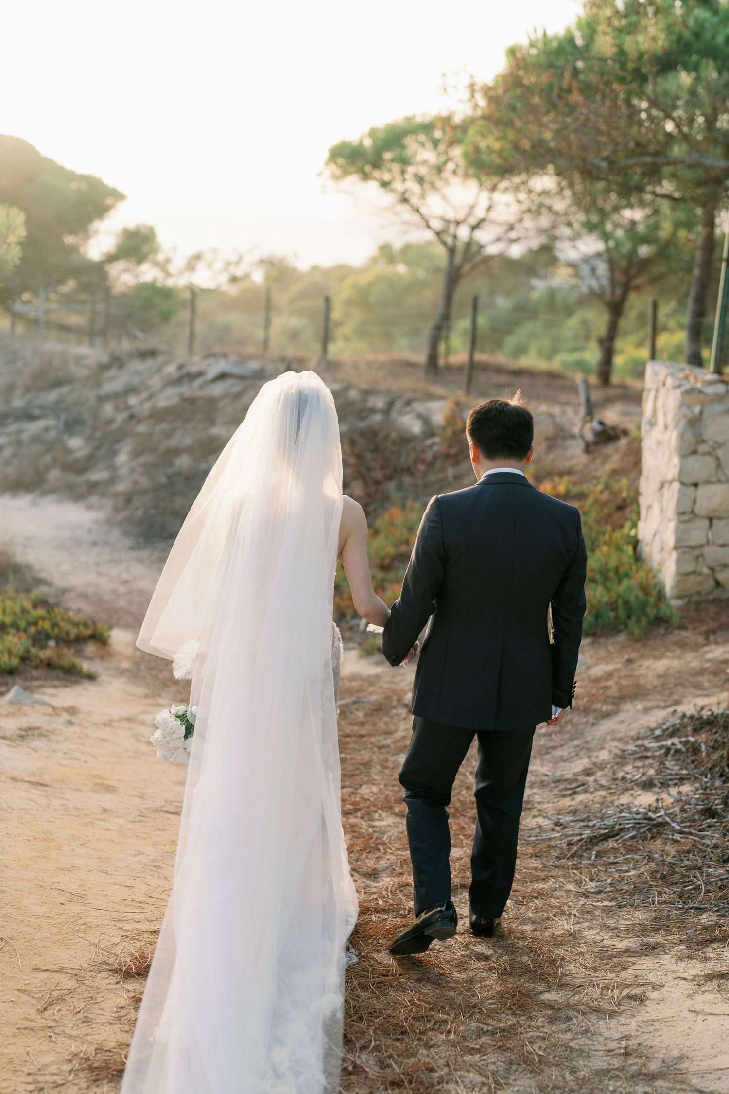 Couple walks along a scenic path during sunset after their wedding ceremony.