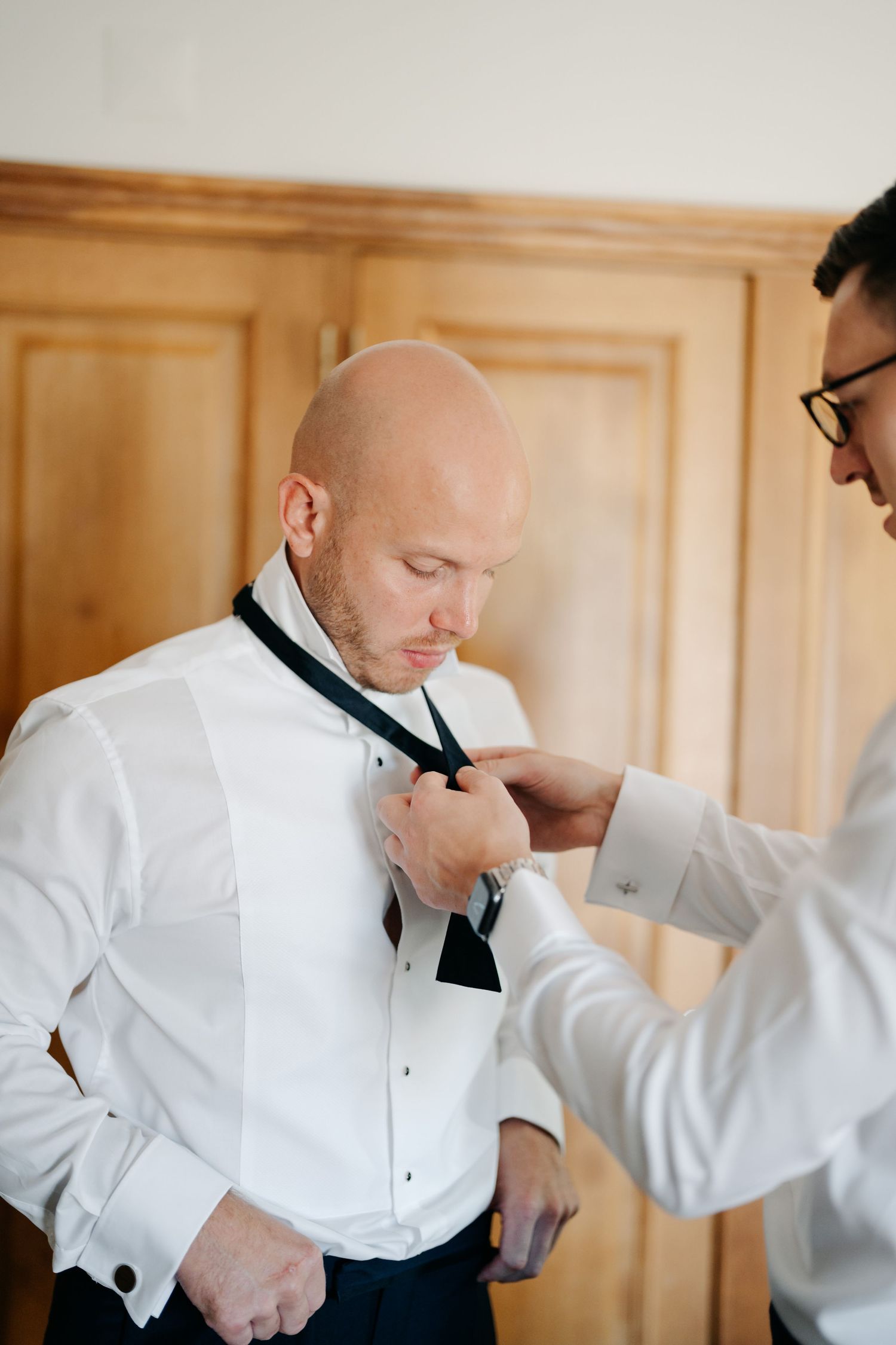 Groomsmen helping adjust a black bow tie on wedding day.