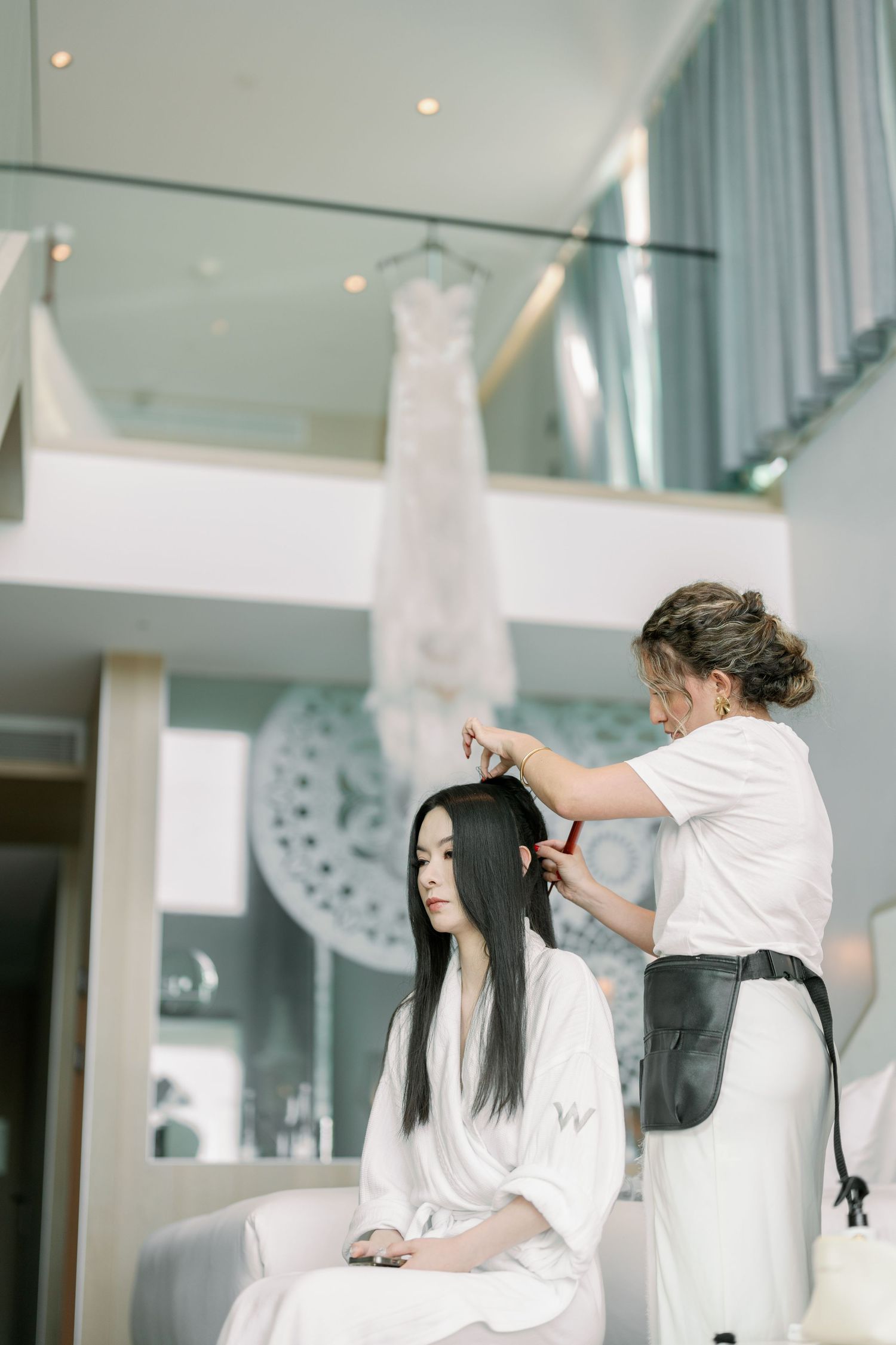 Wedding preparation scene with stylist doing bride's hair in modern interior.