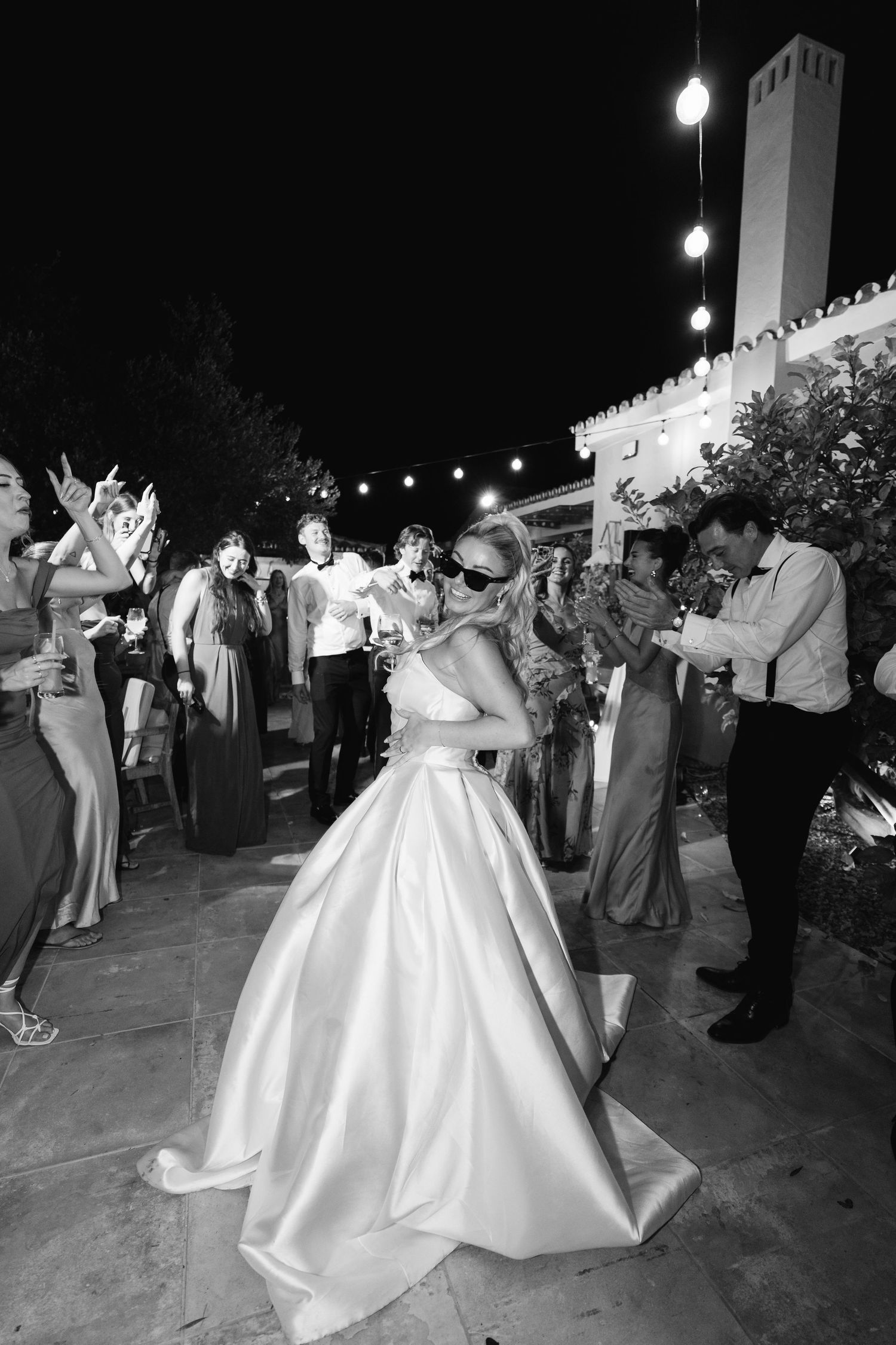 Joyful dancing and celebration at an outdoor wedding reception under string lights.