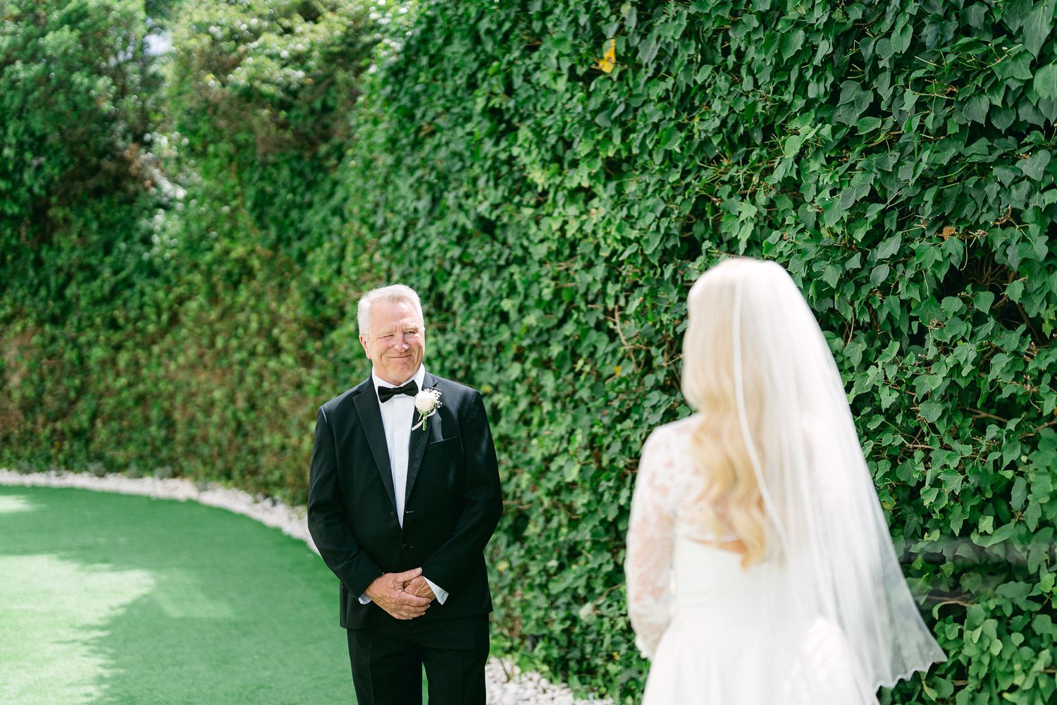 A wedding first look moment captured against a lush green ivy wall backdrop.