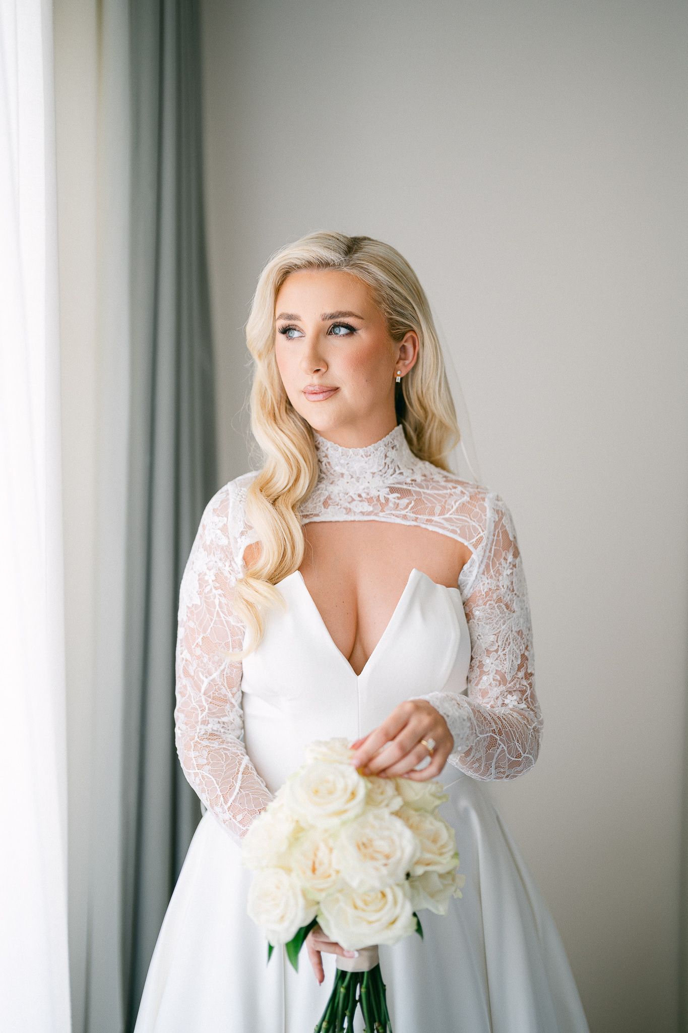 Close-up details of a white wedding dress with lace sleeves and a bouquet of white roses.