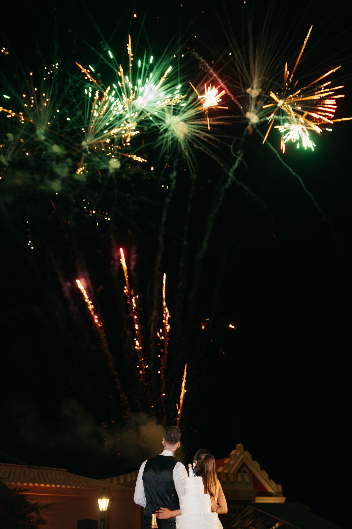 Green and gold fireworks burst dramatically over a wedding venue at night.