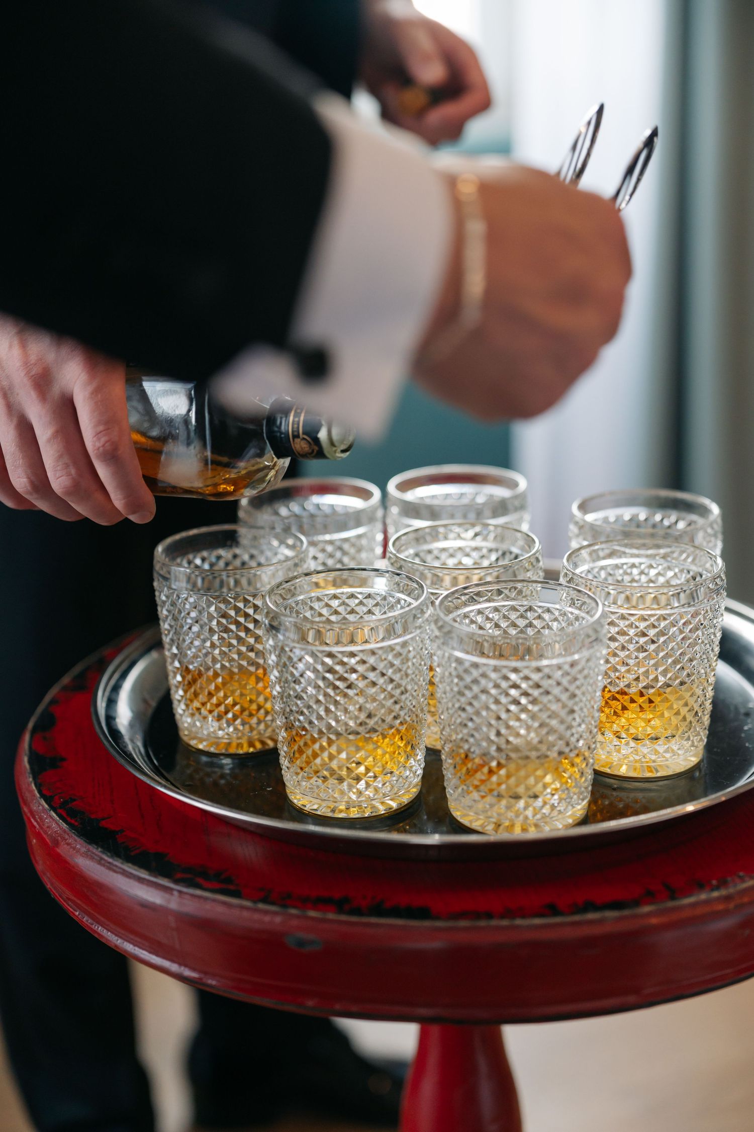 Crystal glasses filled with whiskey on a red serving table.