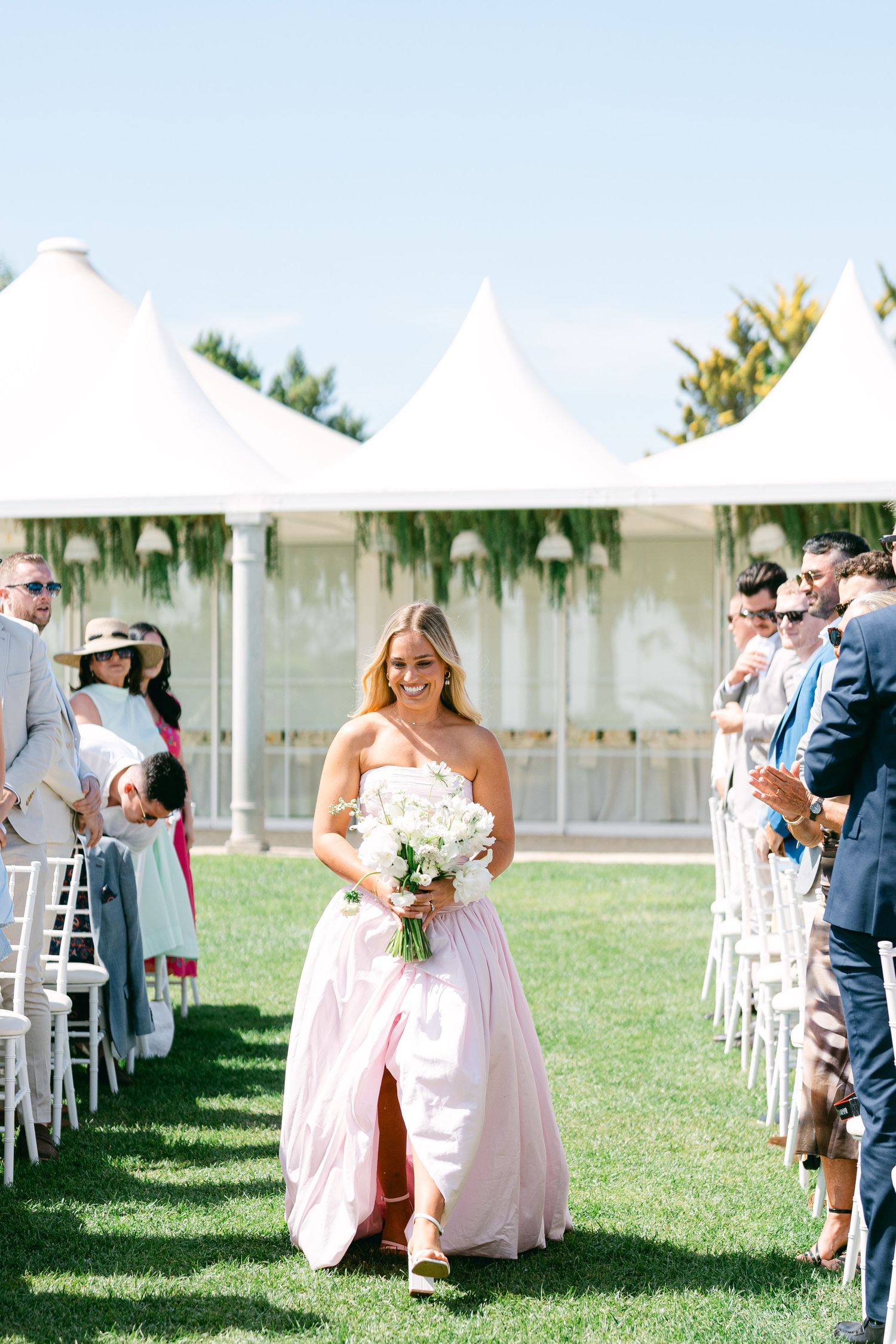 Outdoor wedding ceremony setup with white tents and chairs on a sunny day.