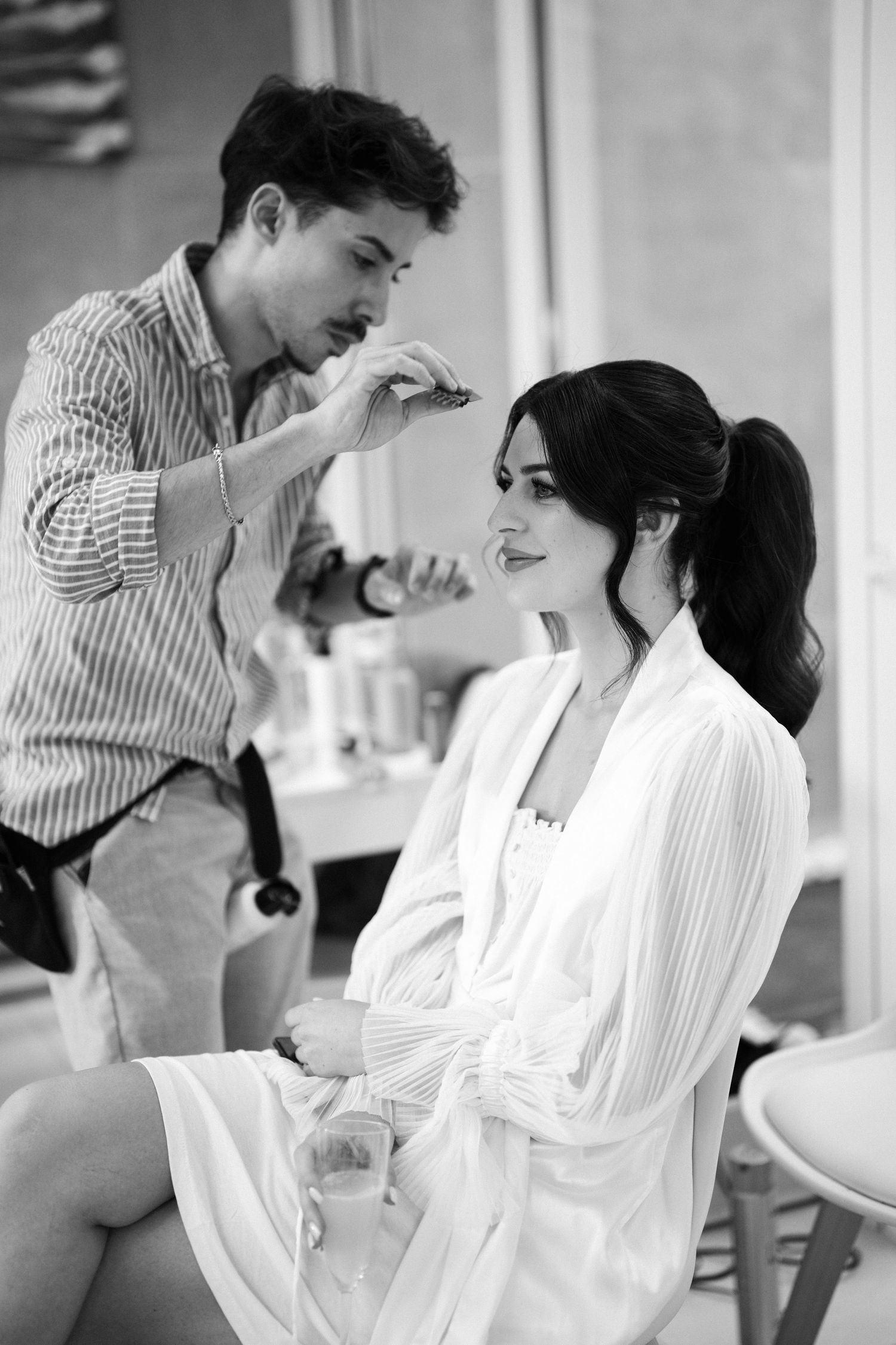 A couple shares a tender moment in black and white as they laugh together in a bright indoor setting.