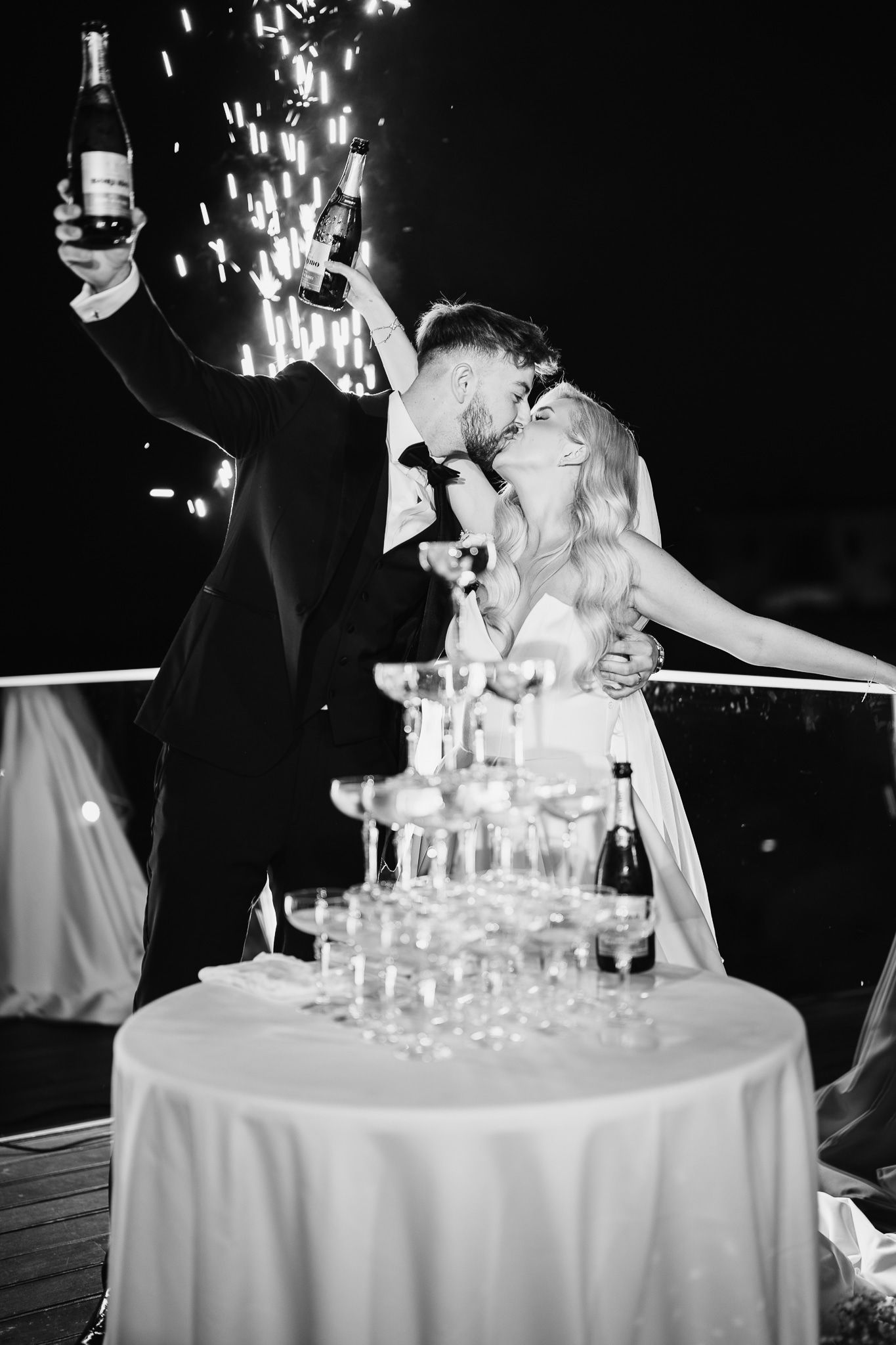 Newlyweds celebrate with champagne tower and sparklers at elegant nighttime wedding reception.