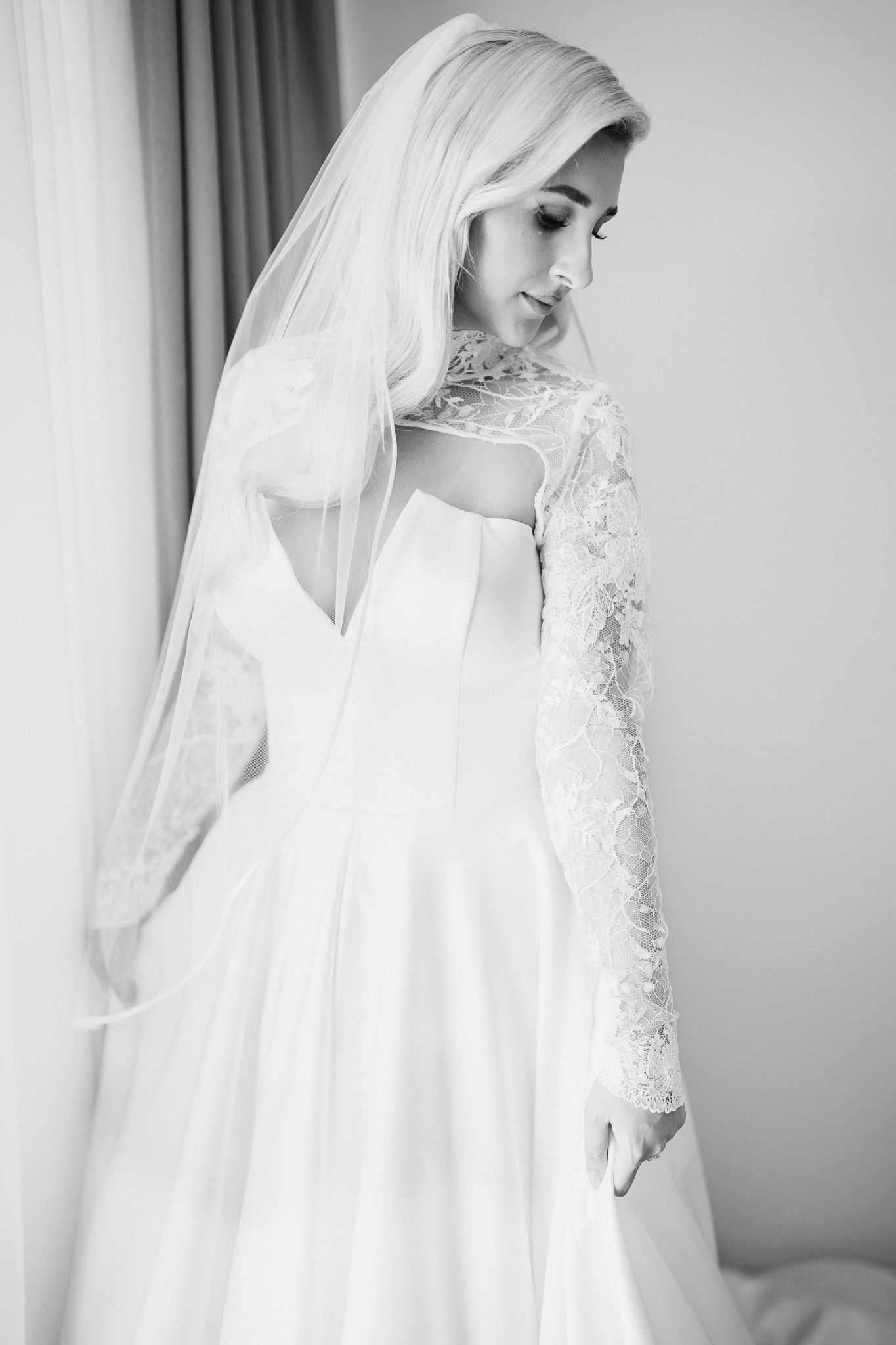Black and white portrait of bride in elegant gown with sheer veil and detailed lace sleeves.