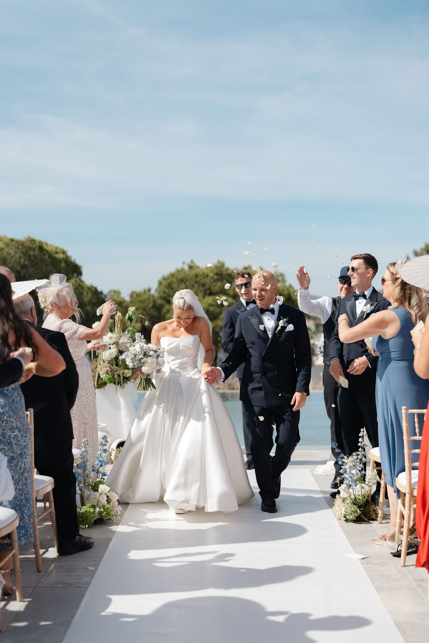 Wedding party and guests celebrating with confetti toss at waterfront venue.