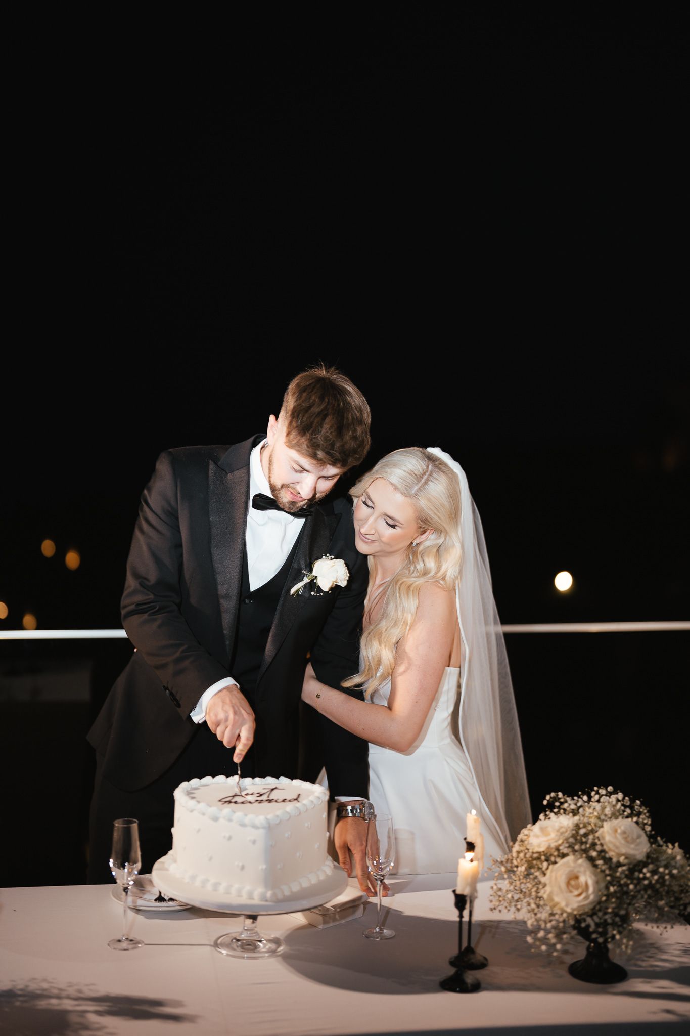 Bride and groom prepare to cut their elegant white wedding cake together.