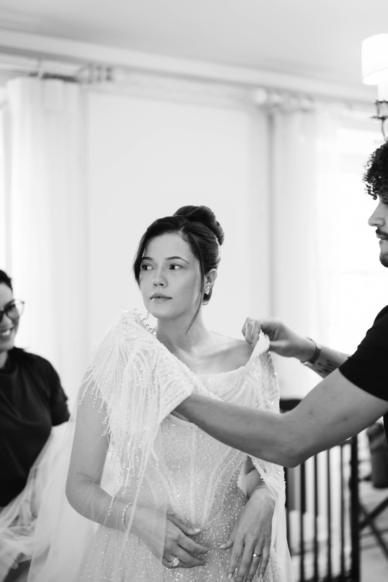 A bride in a white lace dress getting final adjustments made to her wedding attire during preparations.