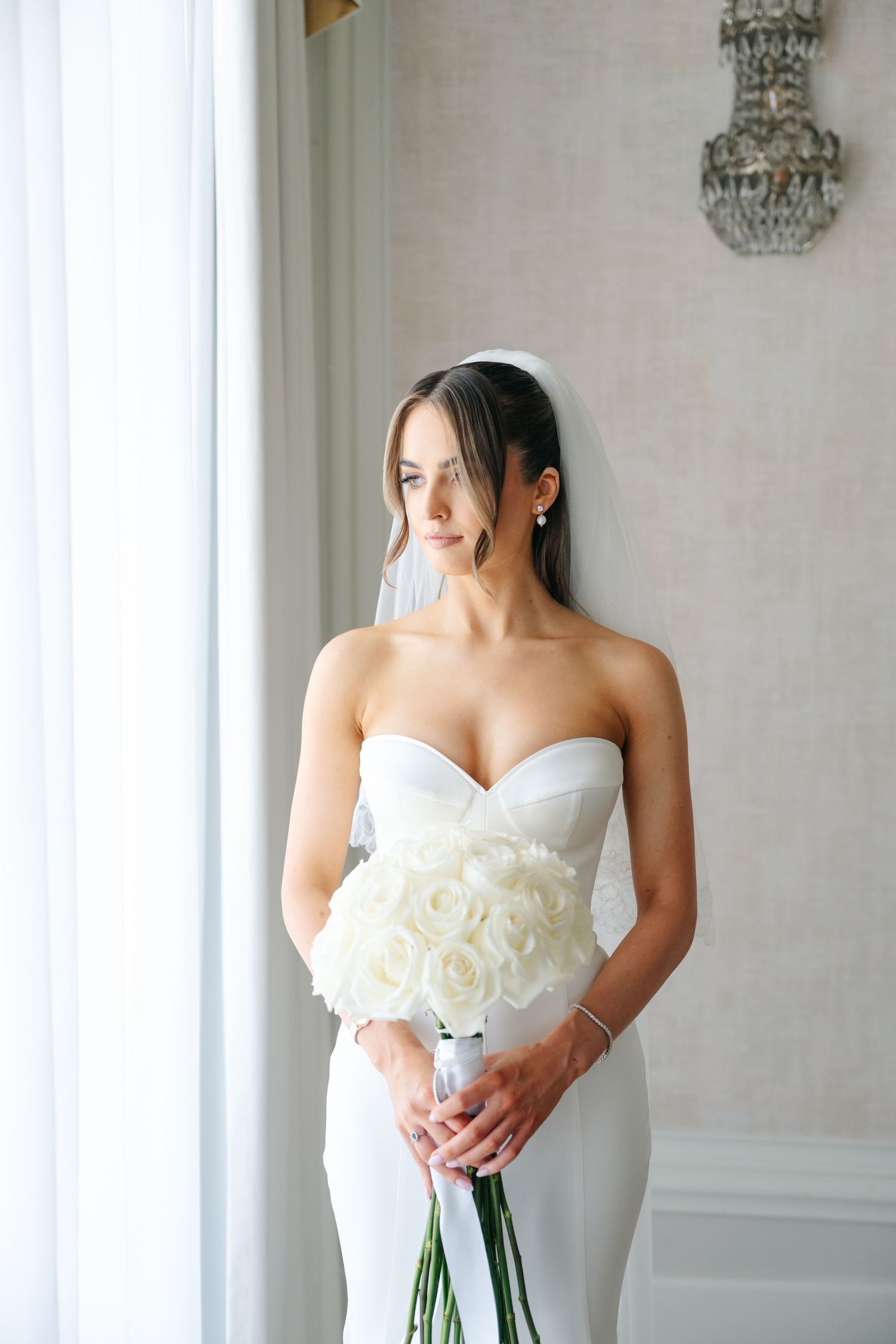 Elegant bride in white strapless gown holding white rose bouquet.