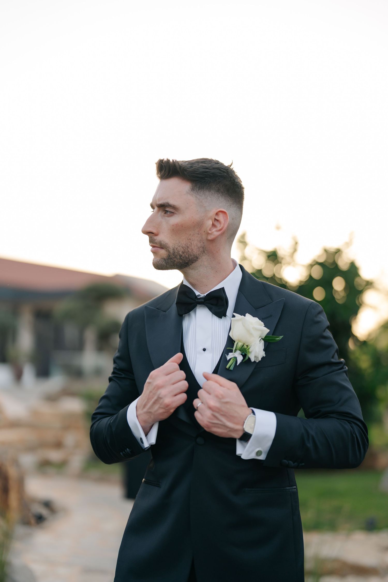 Groom adjusts his tuxedo jacket during outdoor wedding photography session.