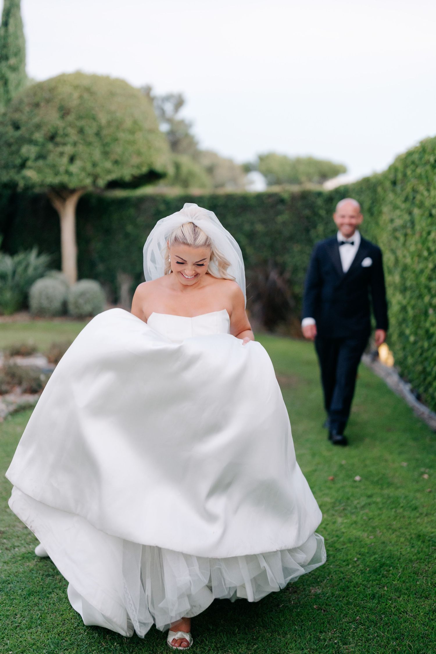Bride's white ballgown flows dramatically as she walks through garden path.