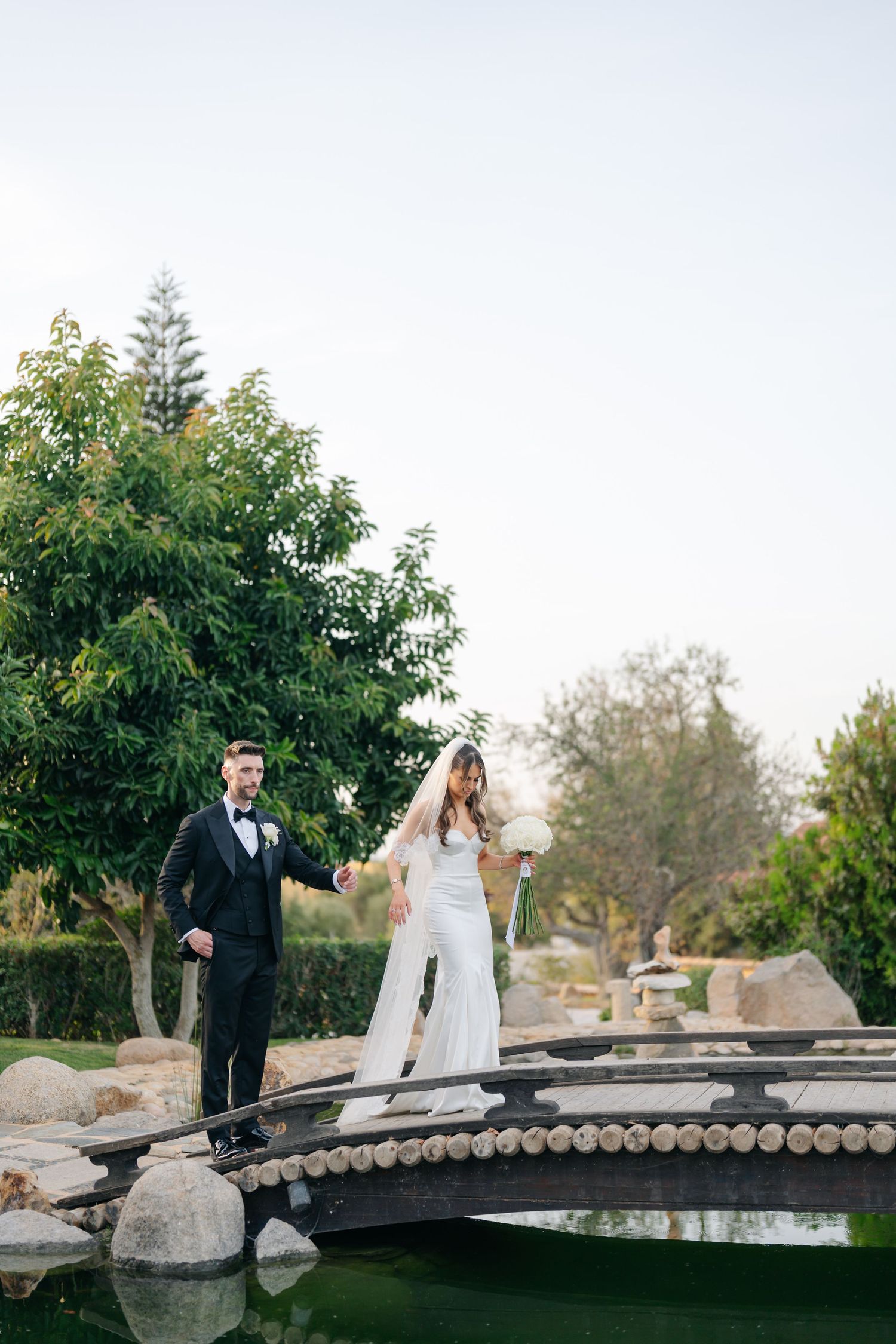 Newlyweds share a romantic moment while crossing an ornate garden bridge.